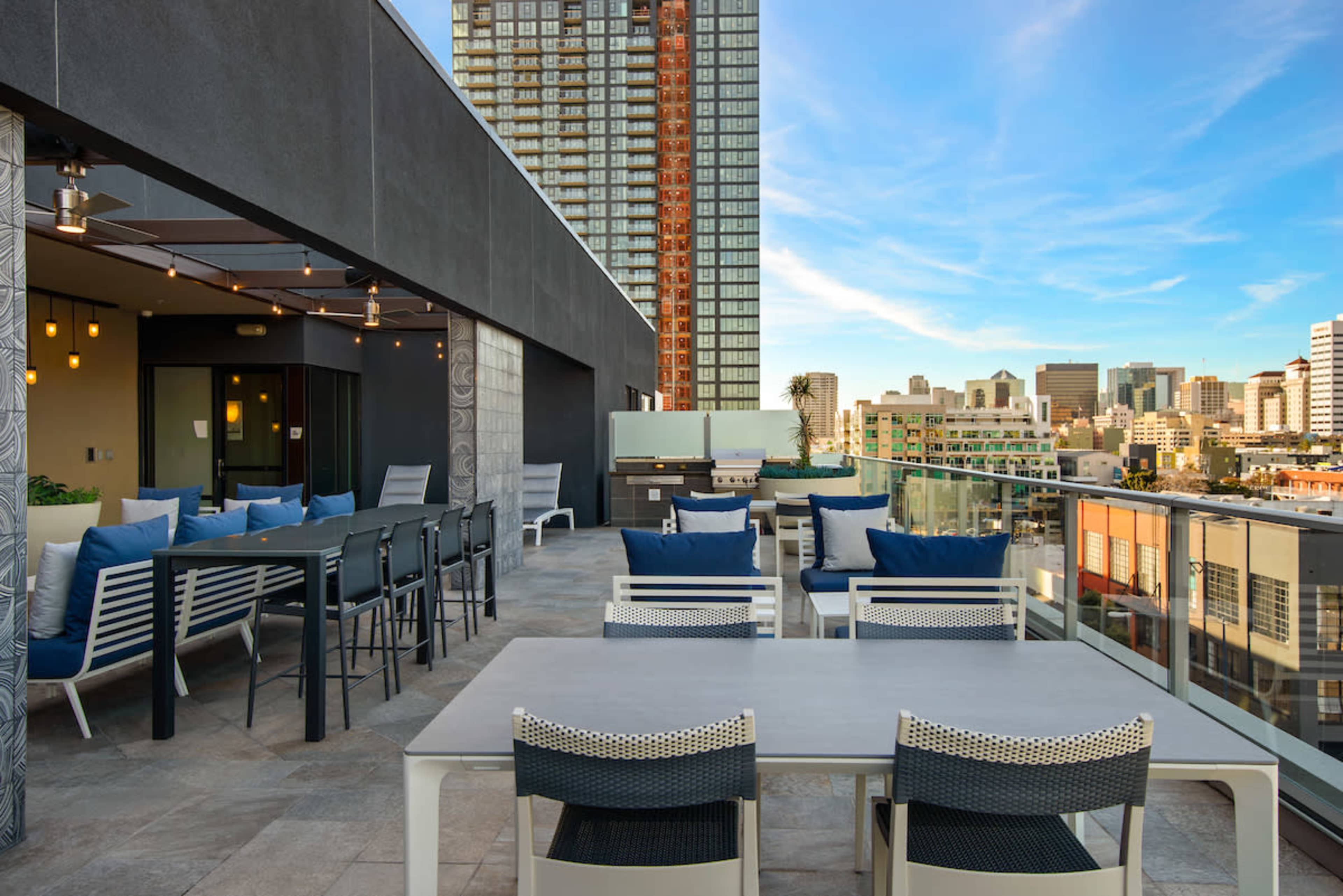 A rooftop terrace featuring modern outdoor furniture, including dining tables and lounge seating, with a city skyline in the background.