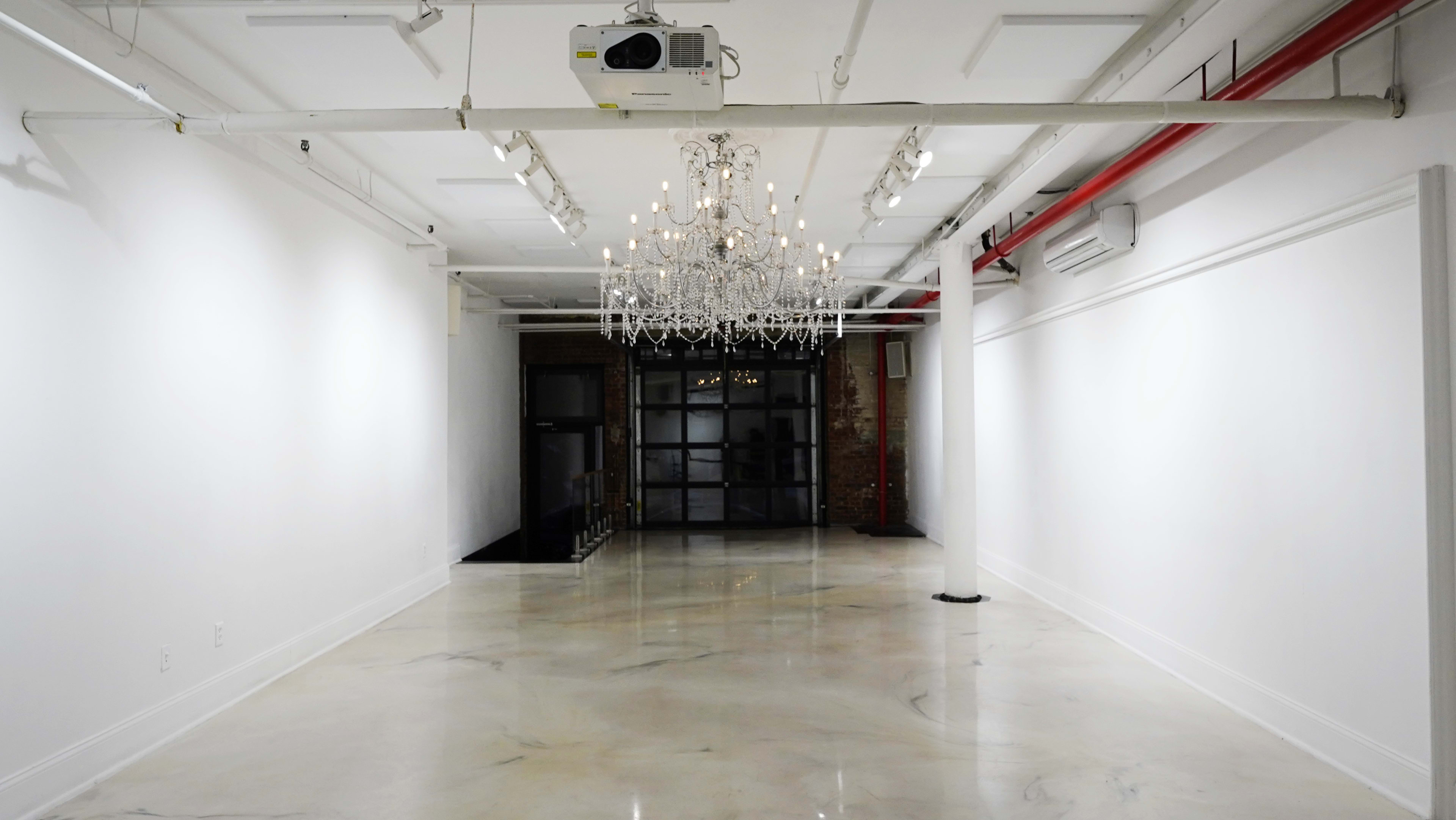 The image shows a spacious interior room with a chandelier hanging from the ceiling and a polished marble floor.