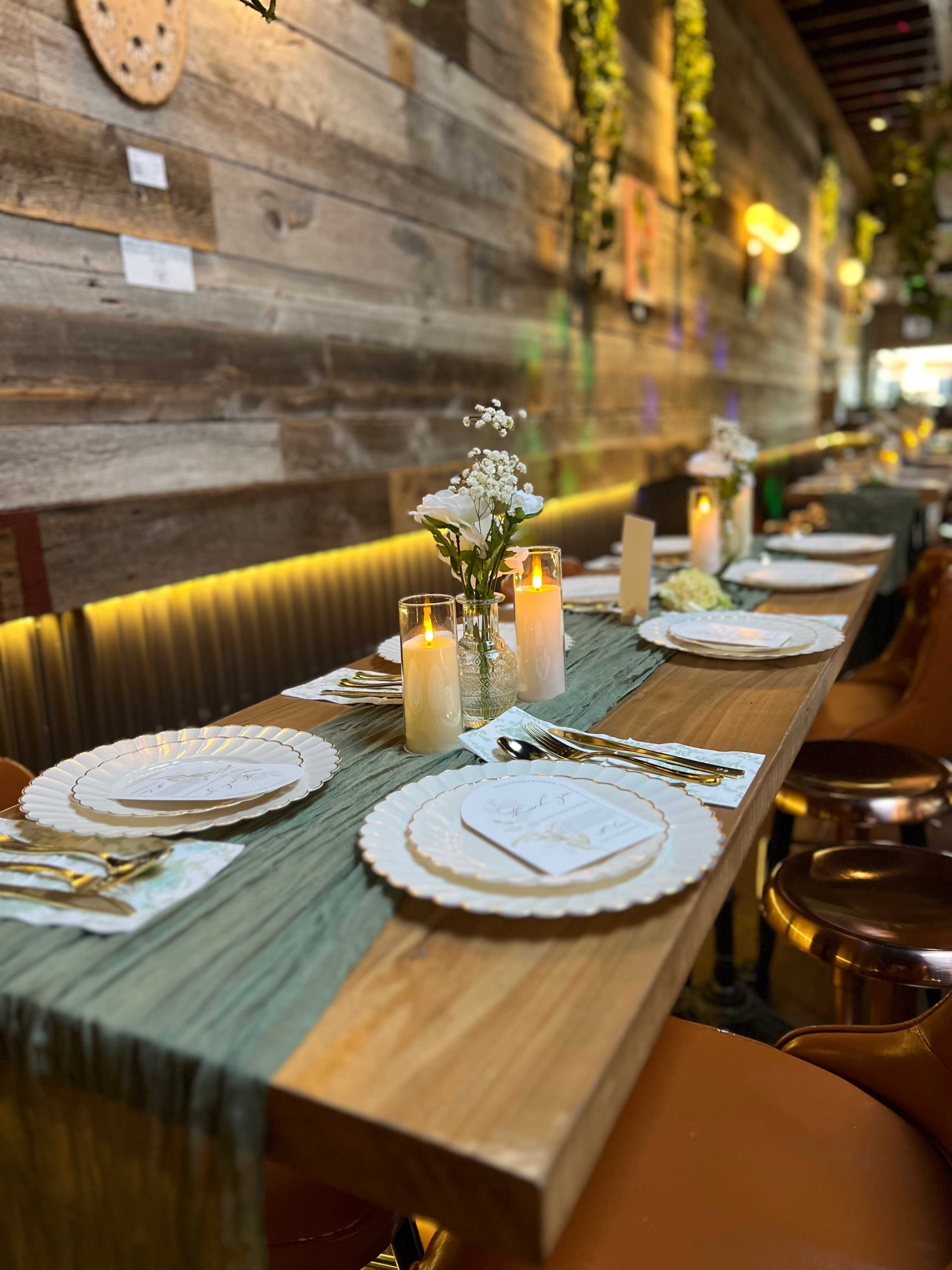 A wooden dining table is set with plates, utensils, and candles, surrounded by modern seating in a rustic restaurant interior.