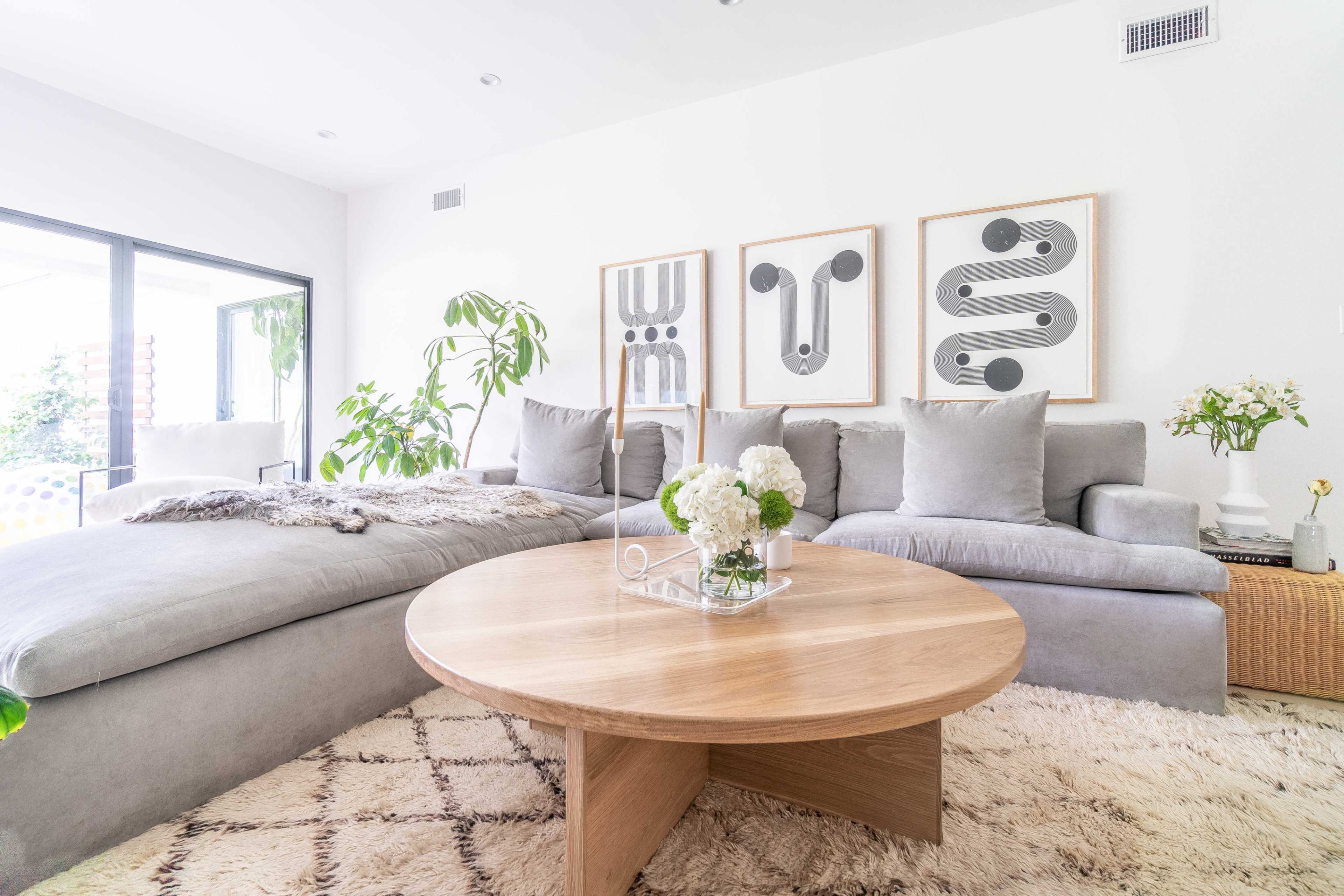 A modern living room features a large sectional sofa, a circular wooden coffee table, and framed abstract art on the walls.