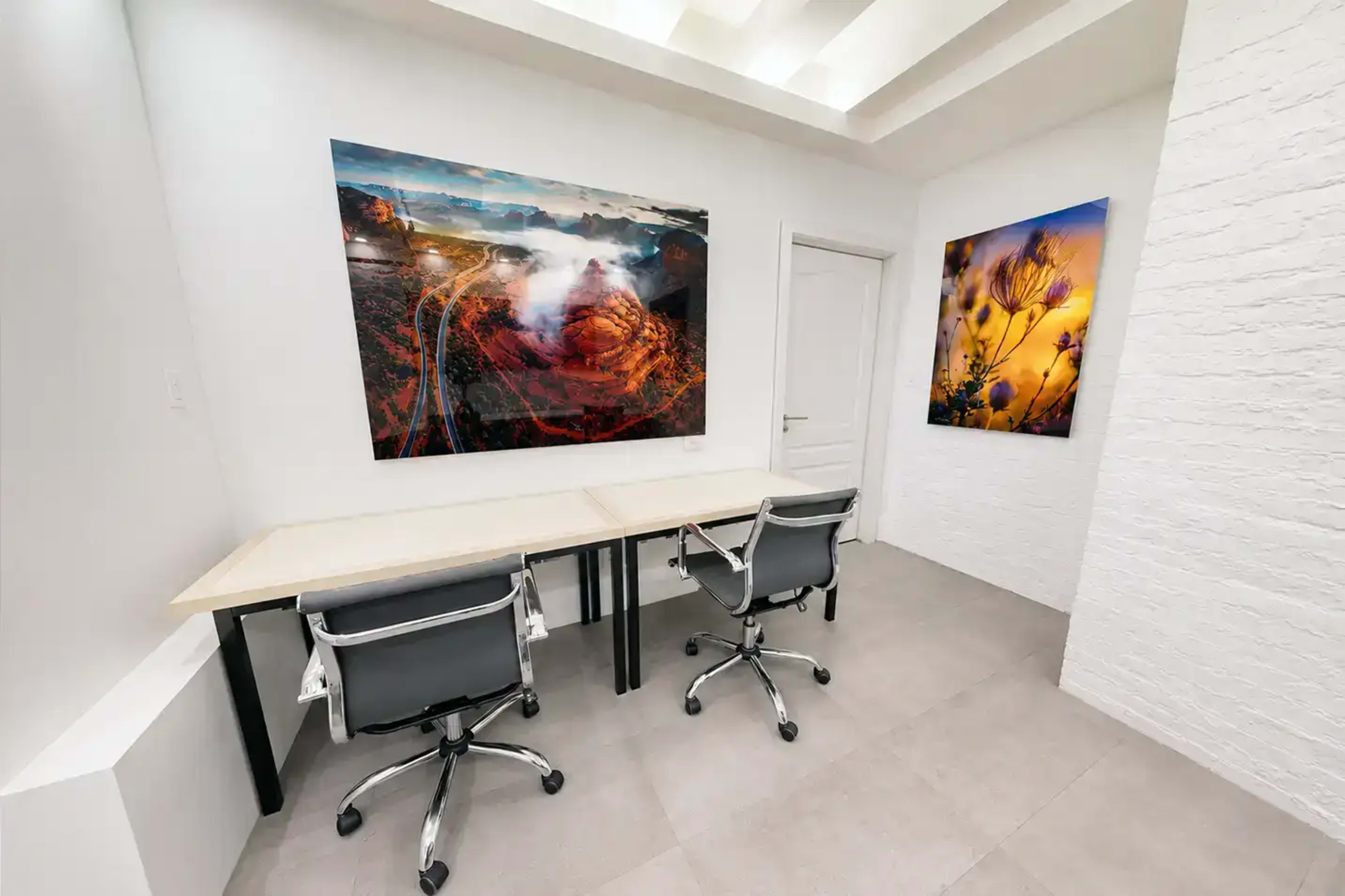 The image features a modern office space with two chairs at a simple desk, flanked by large, framed landscape photographs on the walls.