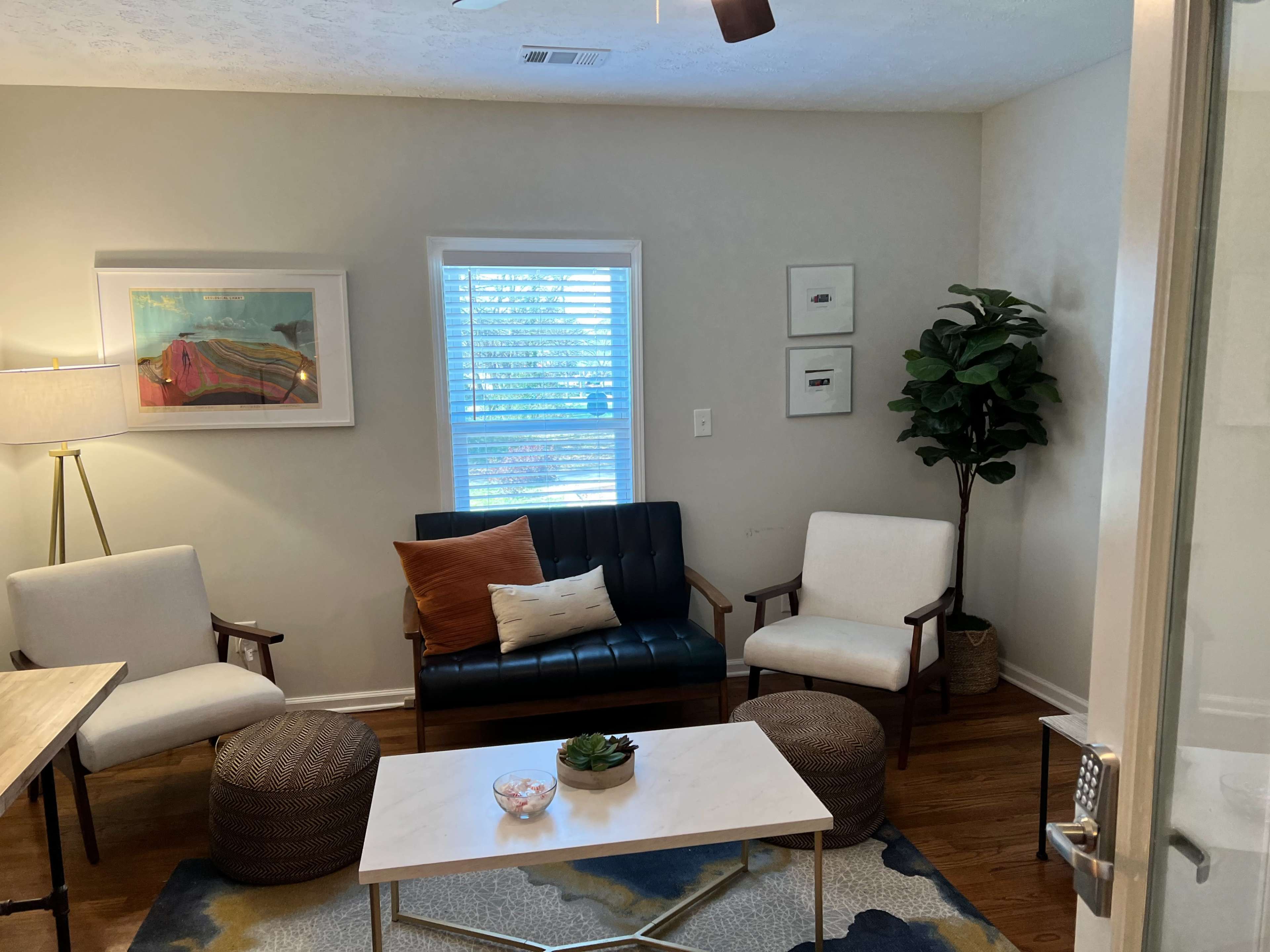 A cozy living room features a mix of seating options, including a dark blue sofa, two white armchairs, and a coffee table on a patterned rug.
