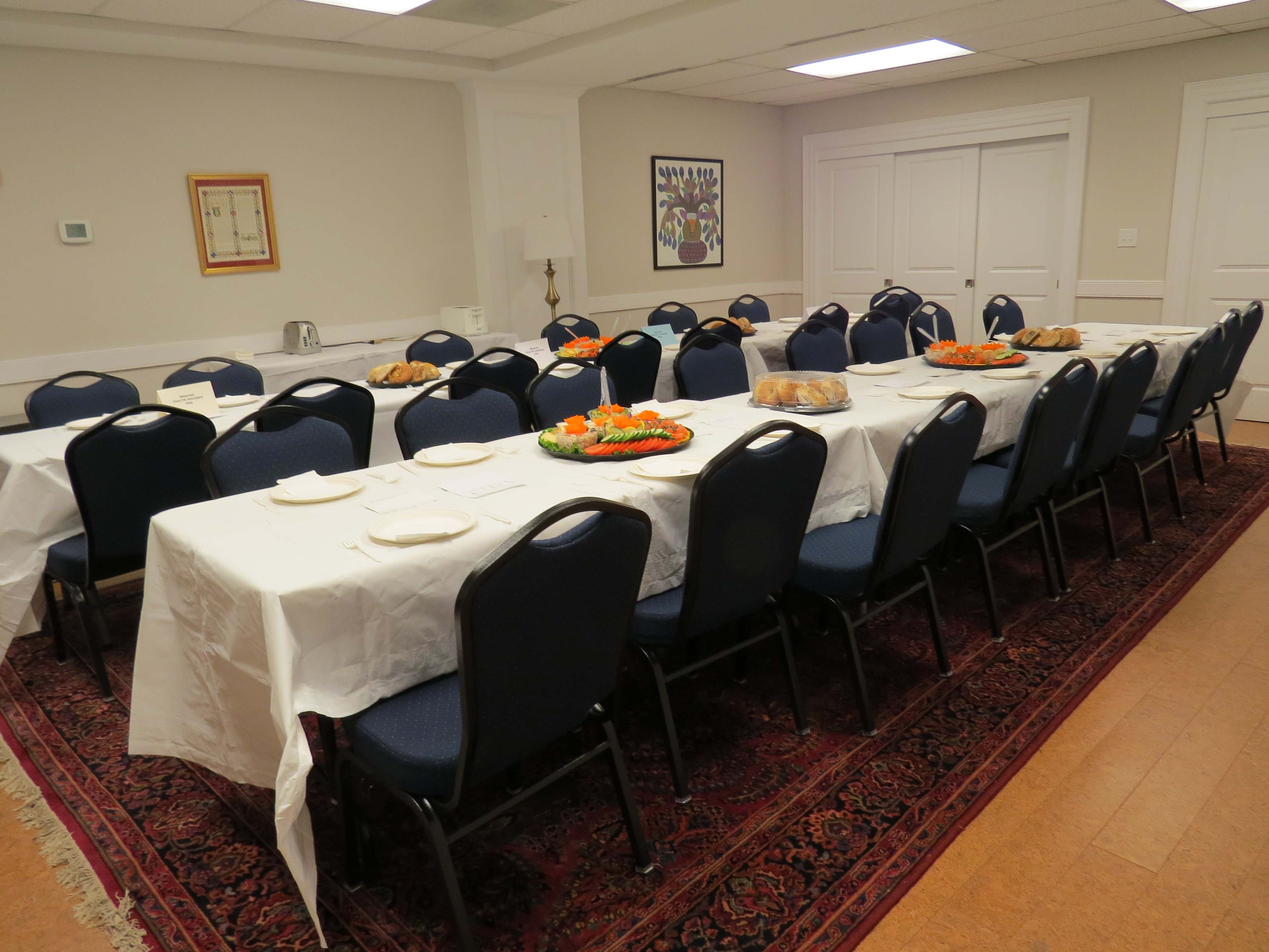 A long dining table is set with white tablecloths, plates, and food platters in a well-lit room.