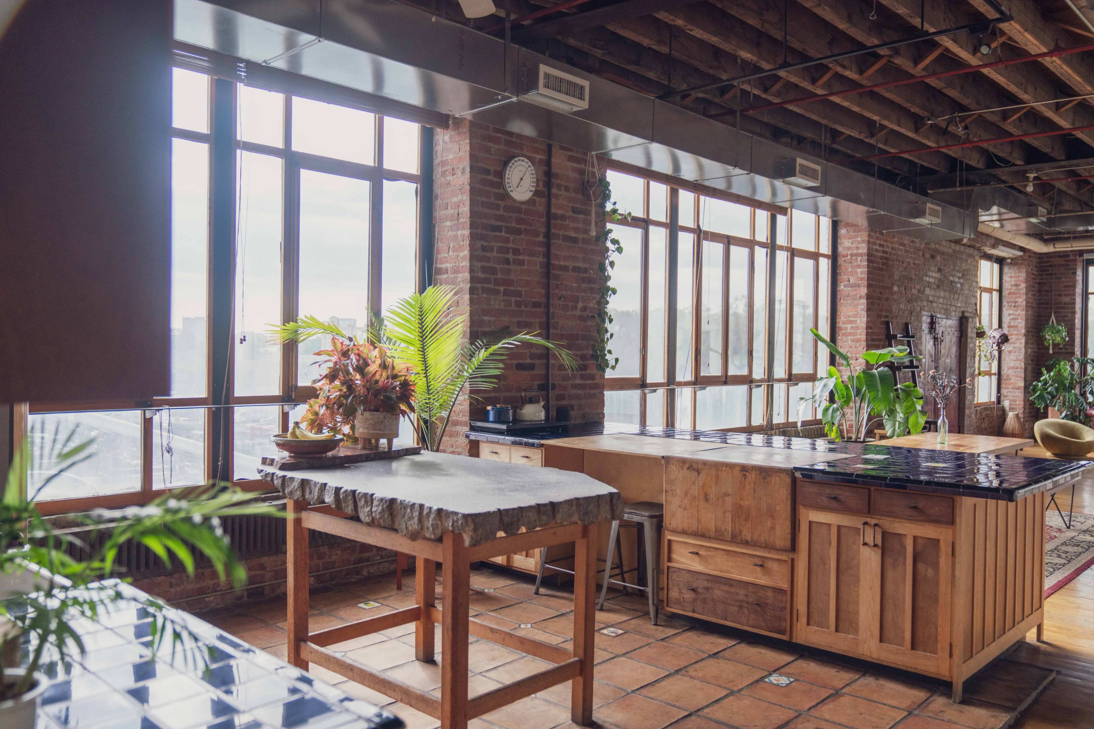 A spacious industrial kitchen with large windows, wooden cabinets, and a stone countertop.