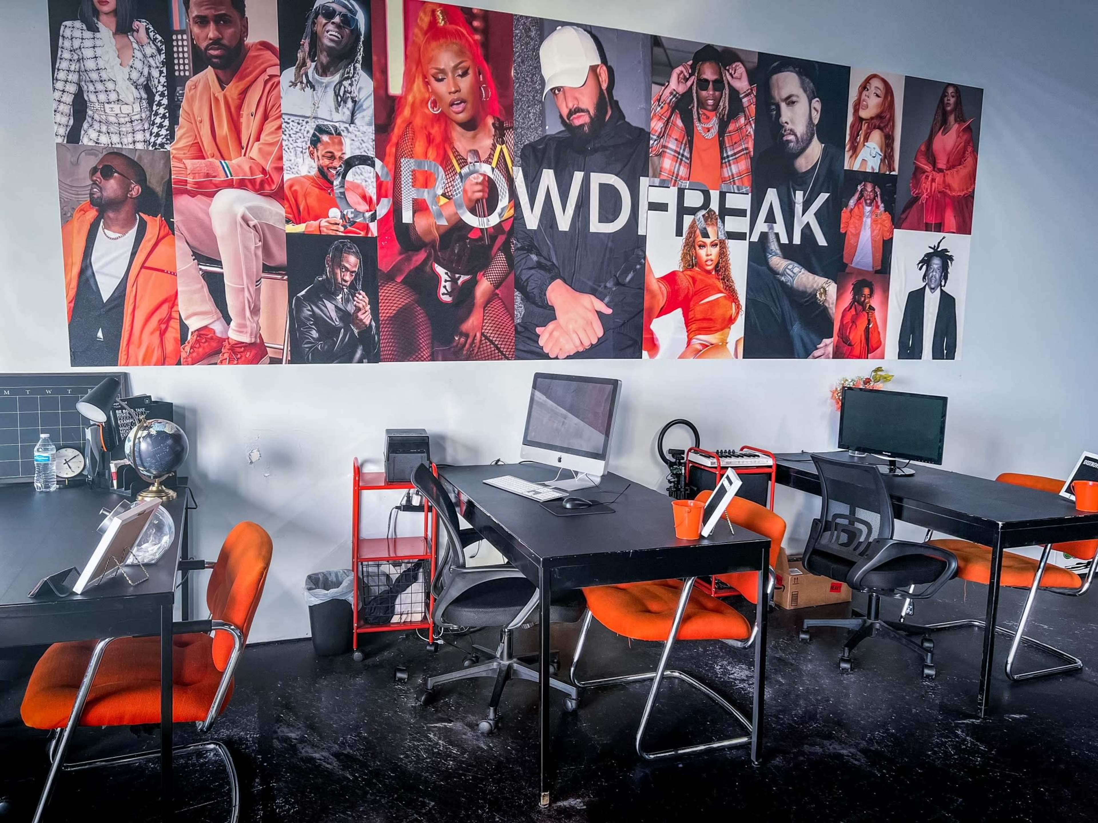 A modern office space with several black tables and chairs, featuring a colorful mural of various artists on the wall.