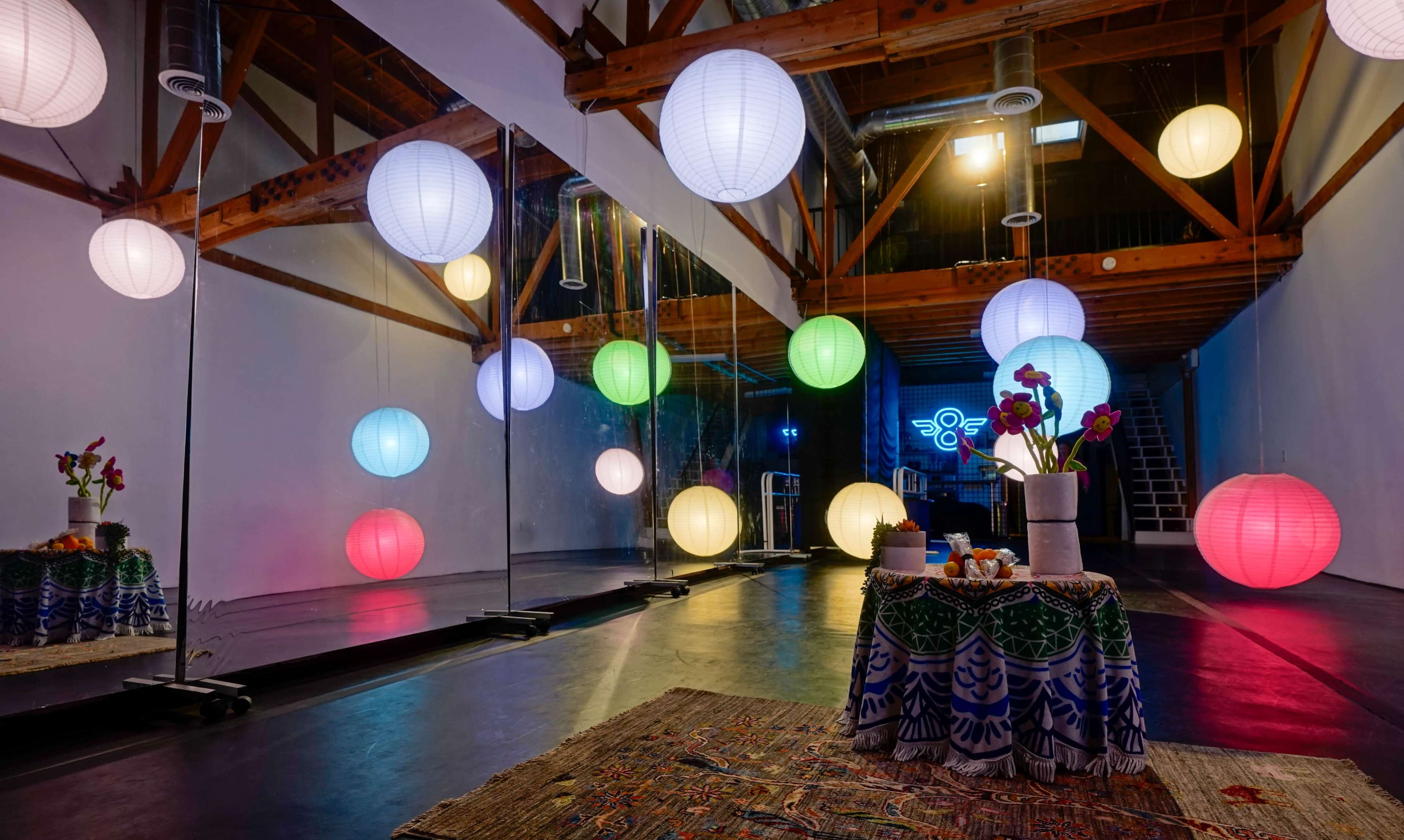 A spacious room features colorful hanging lanterns, mirrors, and a decorative table with flowers and items at its center.