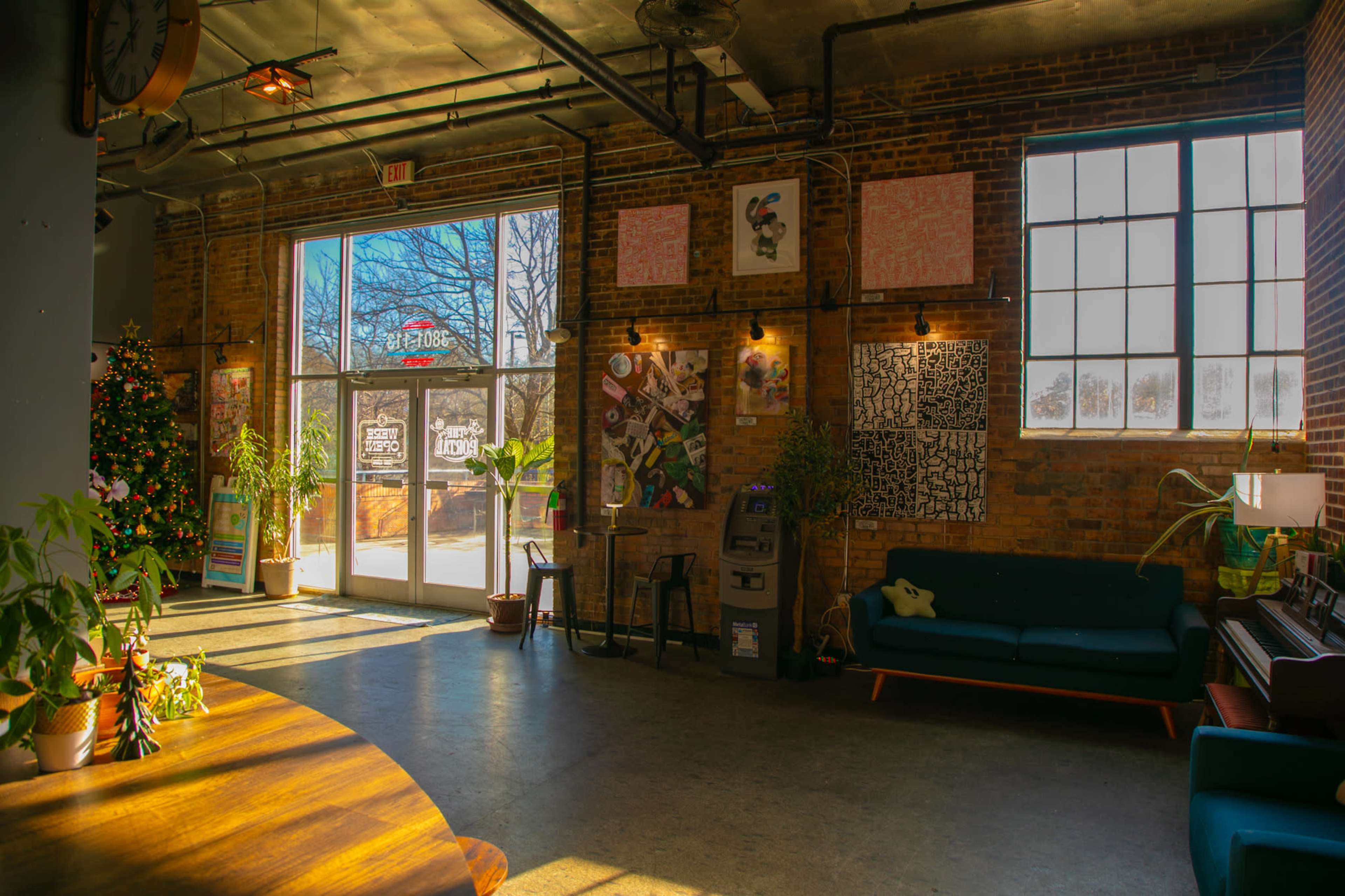 The image shows an interior space with exposed brick walls, a large window, a seating area with a couch, and various artworks displayed.