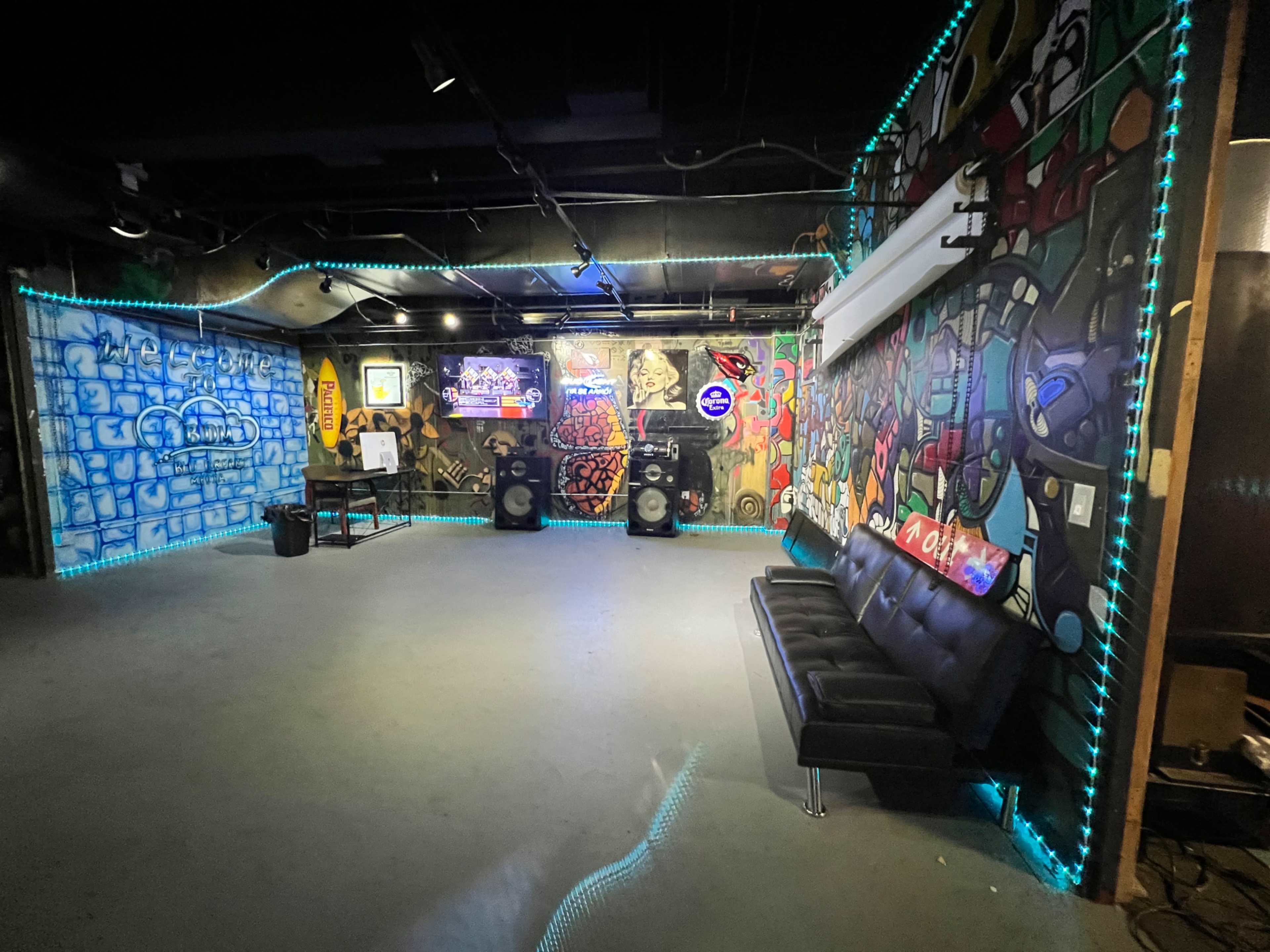 The image shows an urban-themed room with colorful graffiti murals, a black couch, and audio equipment placed against the walls.