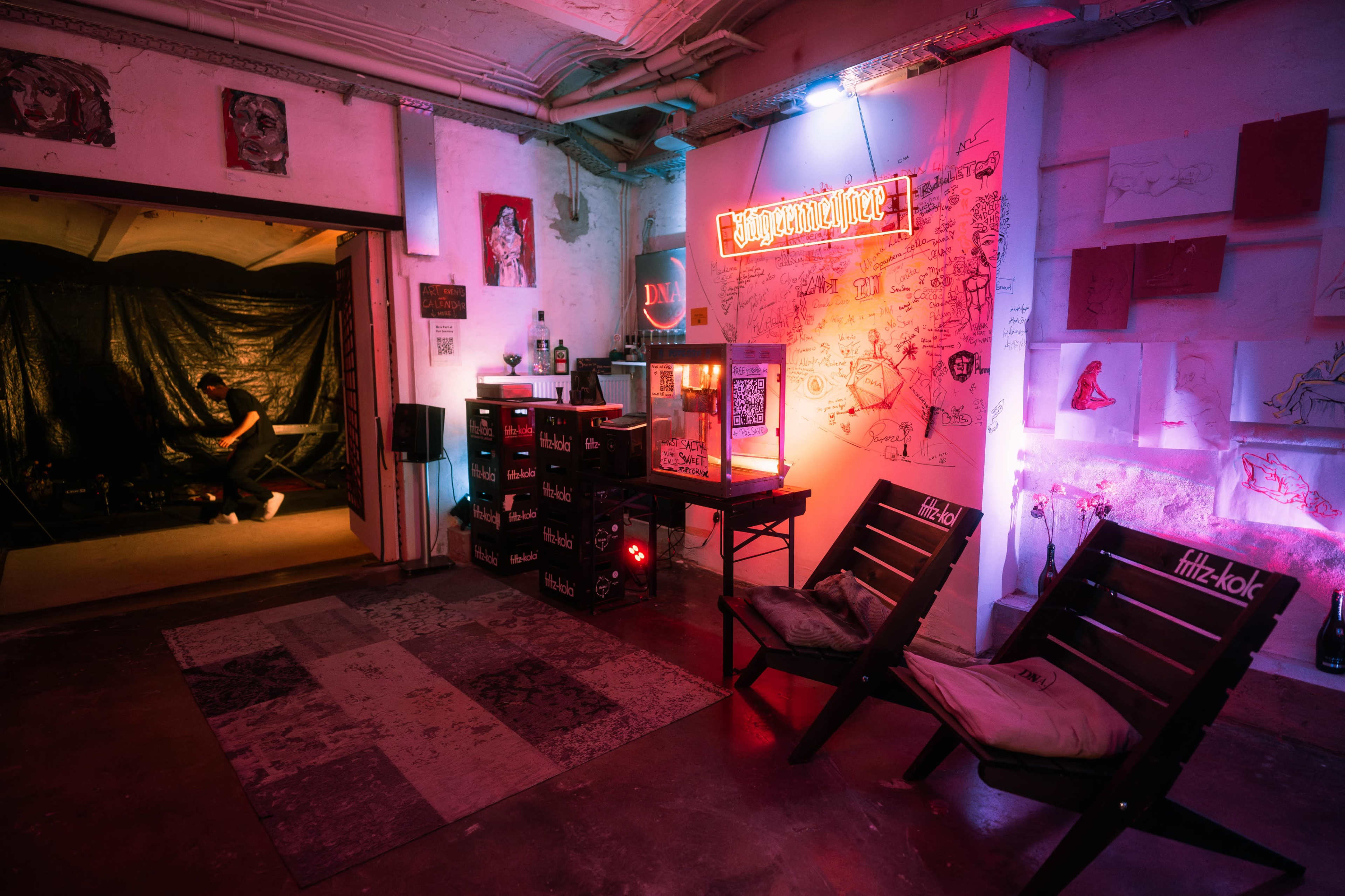 The image shows a creatively designed room featuring colorful neon lights, a vintage popcorn machine, and artistic wall decorations, with a person sitting in the background.