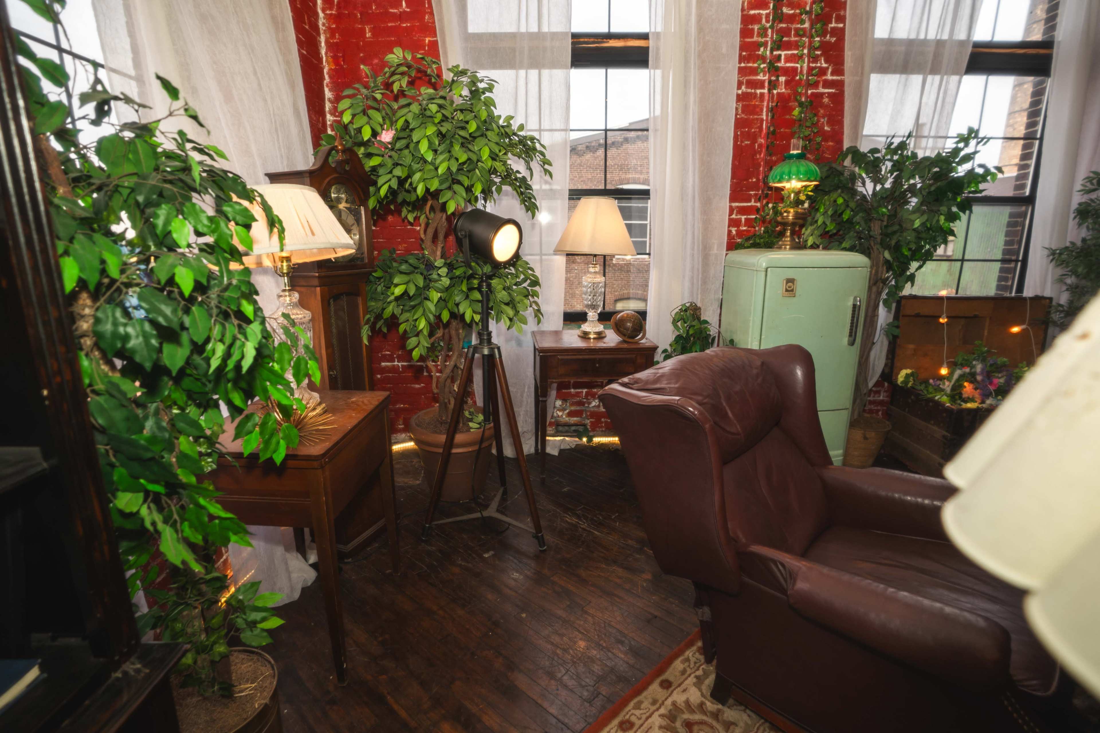 The image features a cozy corner of a room with brick walls, plants, vintage lamps, a brown leather armchair, and a green retro refrigerator.