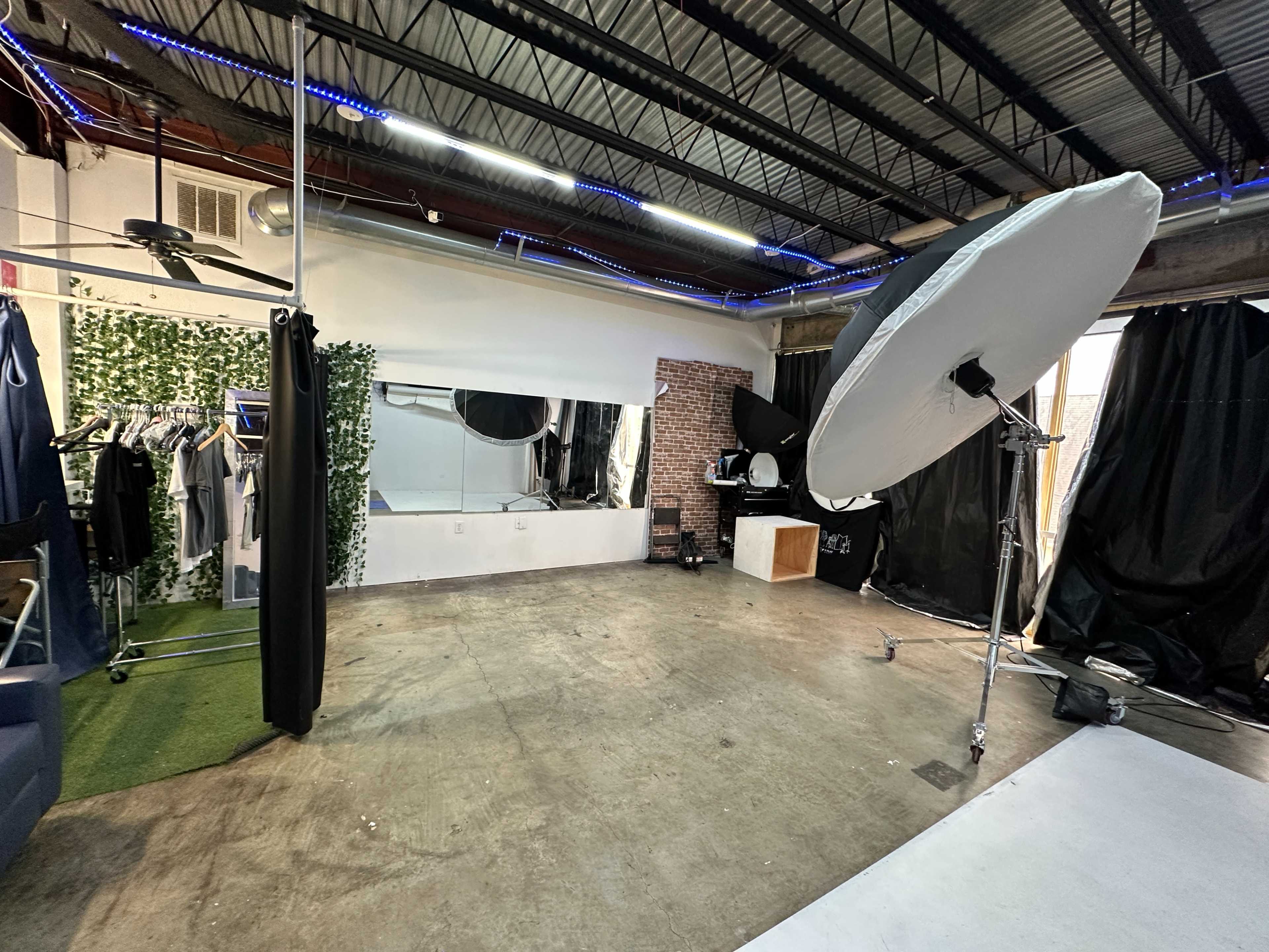 A studio space with a section of mirrored wall, hanging clothing racks, a large light source on a stand, and black curtains in the background.