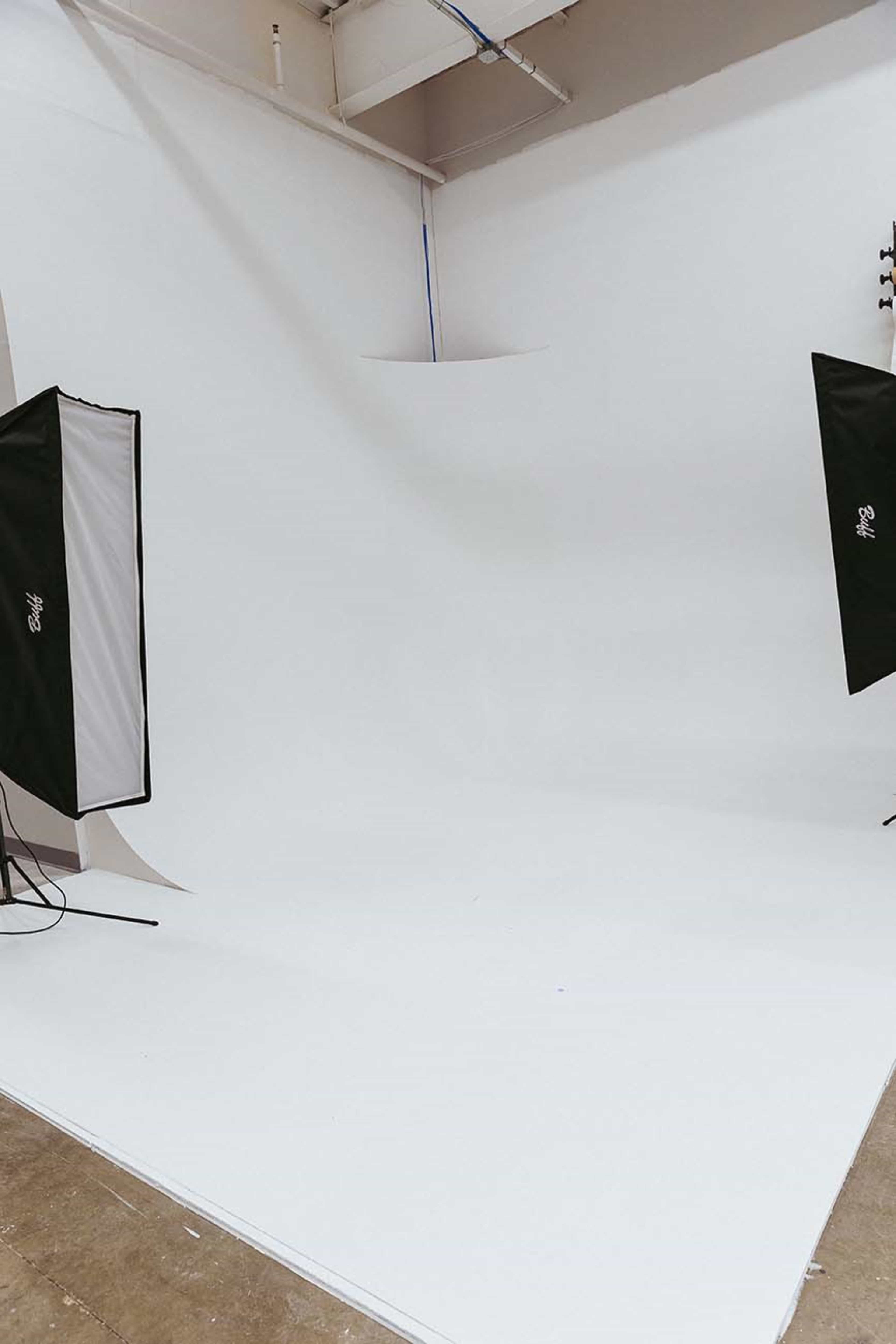 The image shows a minimal photography studio with a white backdrop and two softbox lighting setups.