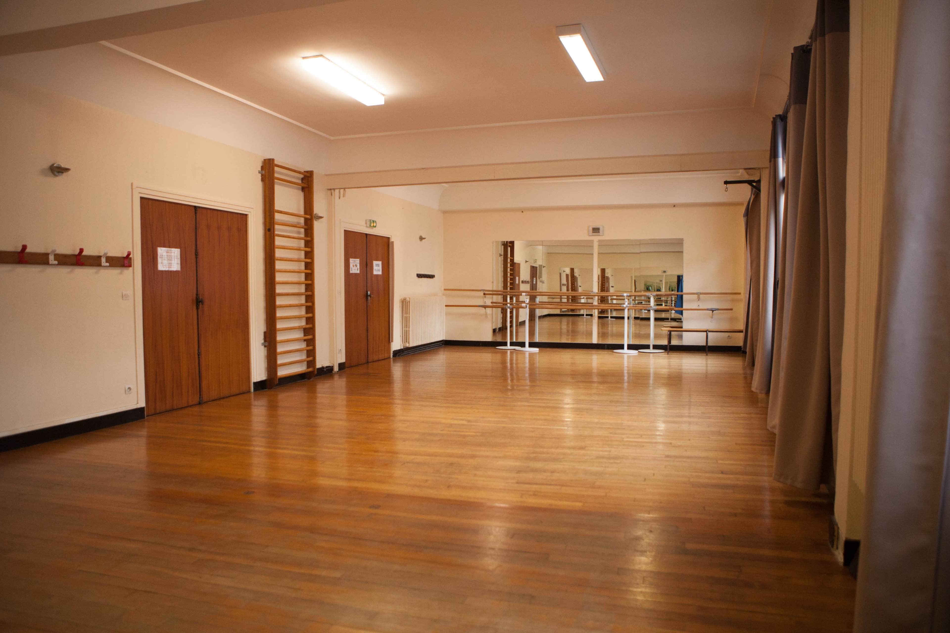 The image shows a spacious wooden-floored dance studio with mirrors and ballet bars along the walls.
