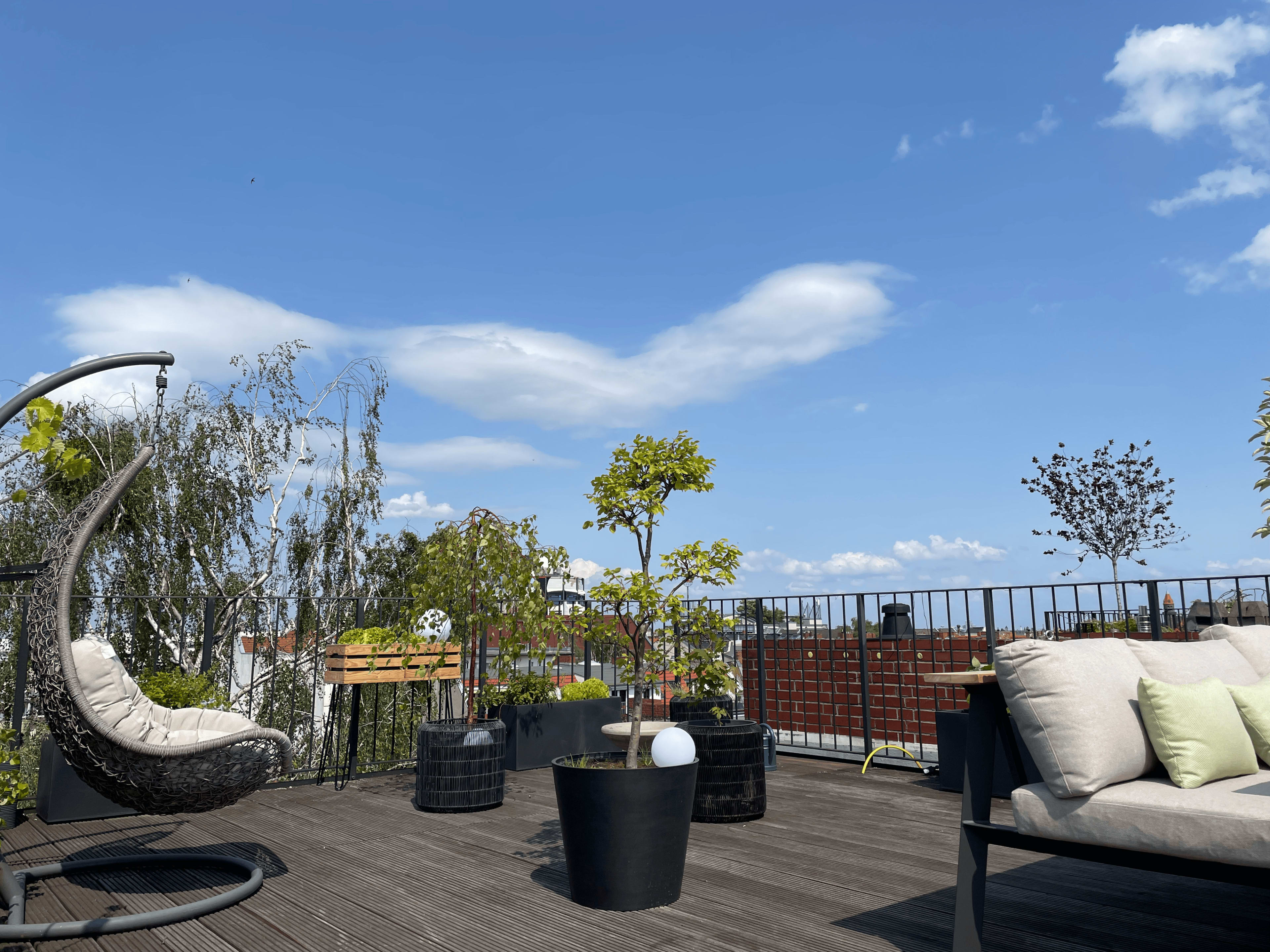 A rooftop terrace features a hanging chair, potted plants, and a clear blue sky with some clouds.
