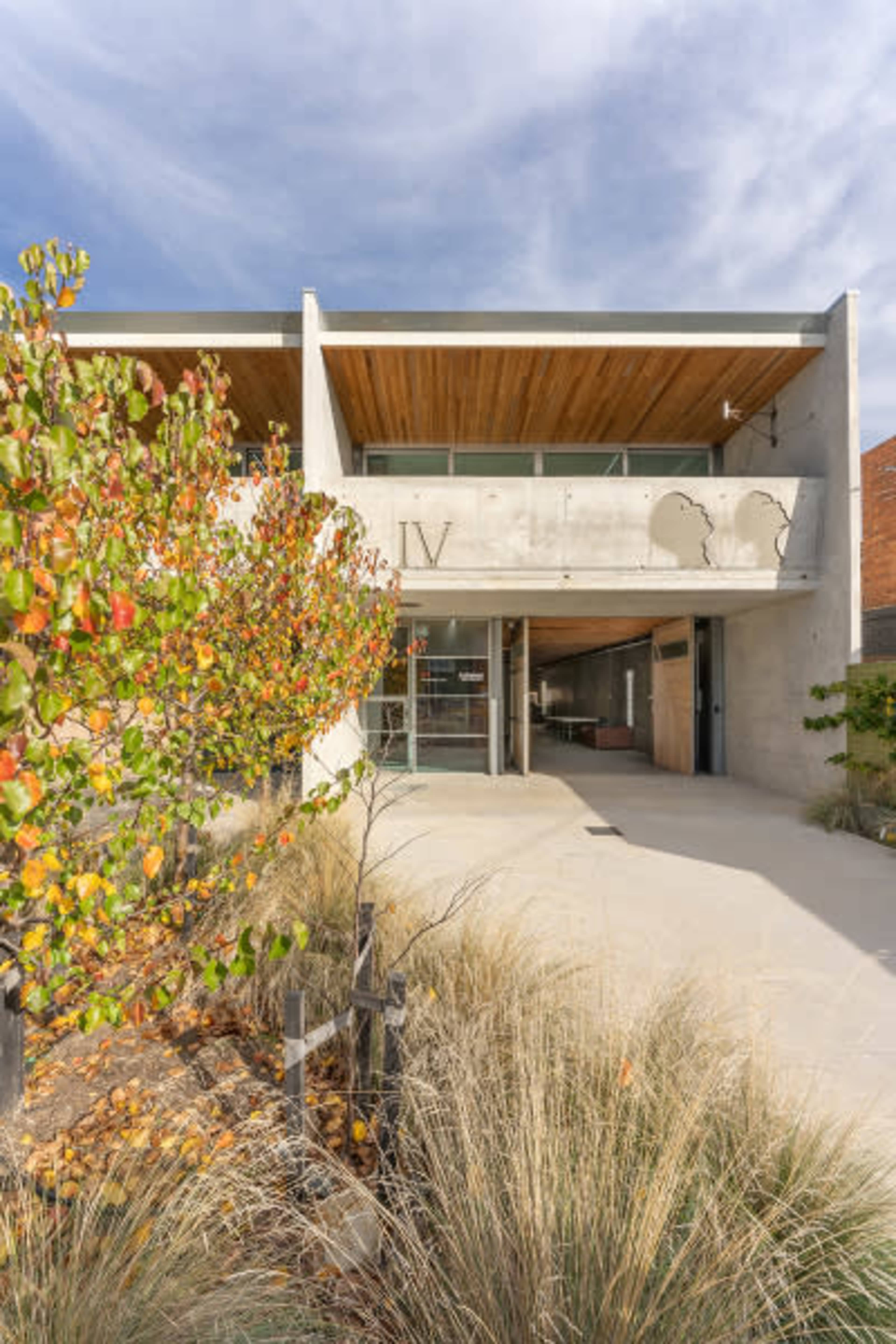 A modern building with a concrete facade and large glass entrance, surrounded by landscaping featuring colorful foliage.