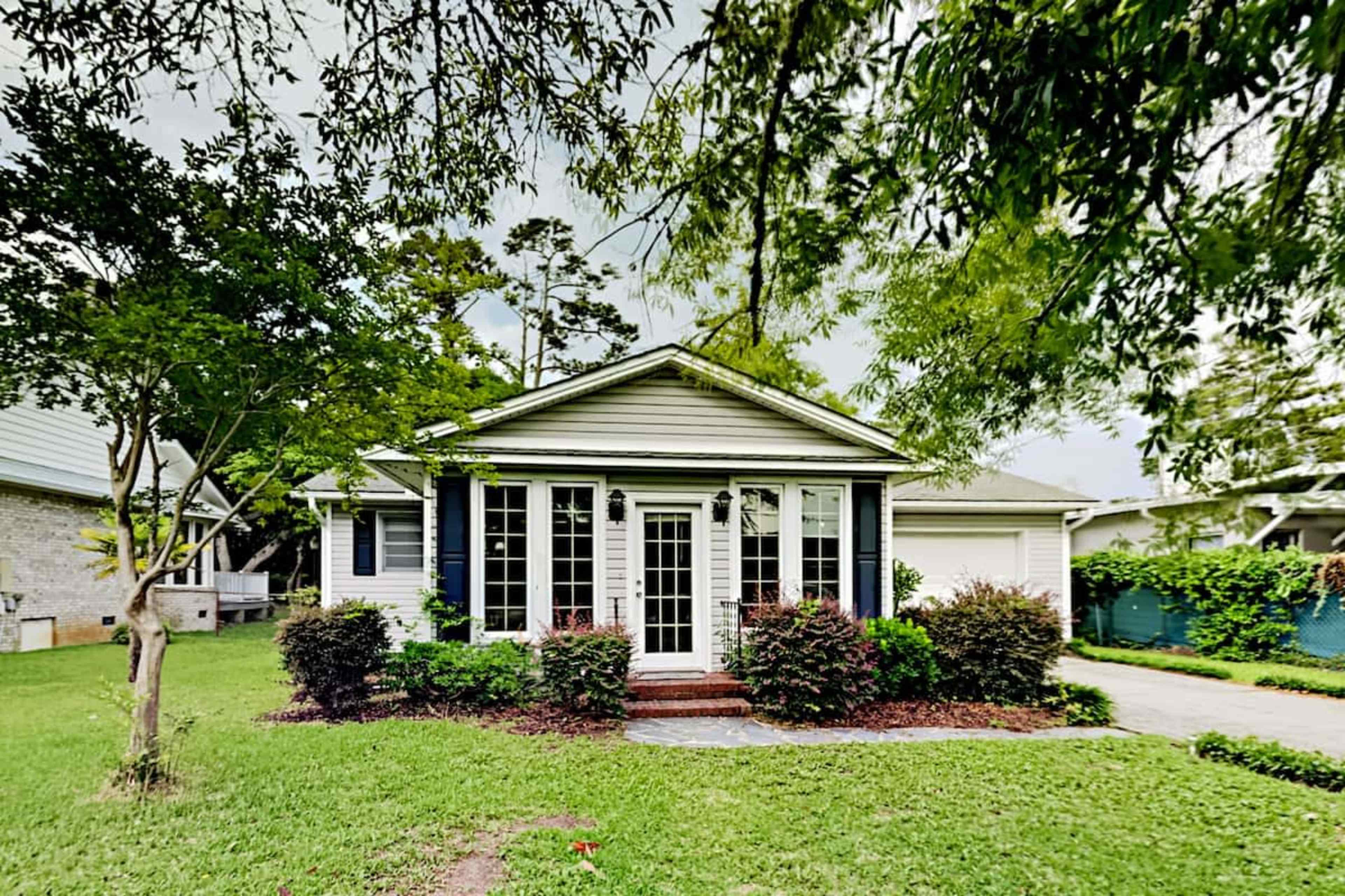 The image shows a single-story house with a front lawn surrounded by trees and shrubs.