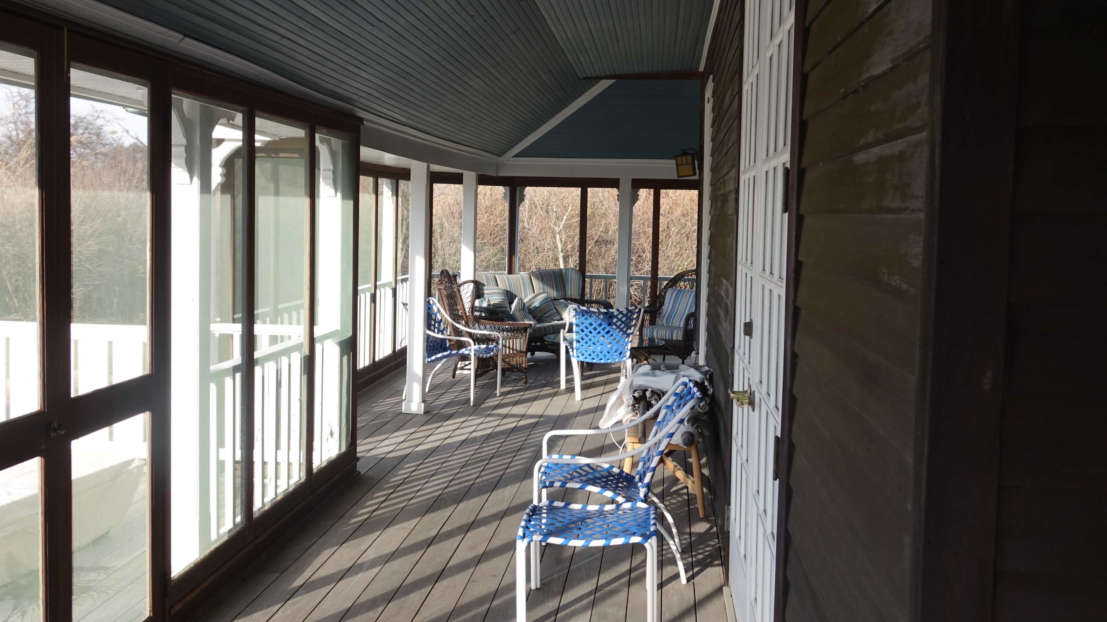 A covered porch with several chairs and tables arranged along the wooden floor.
