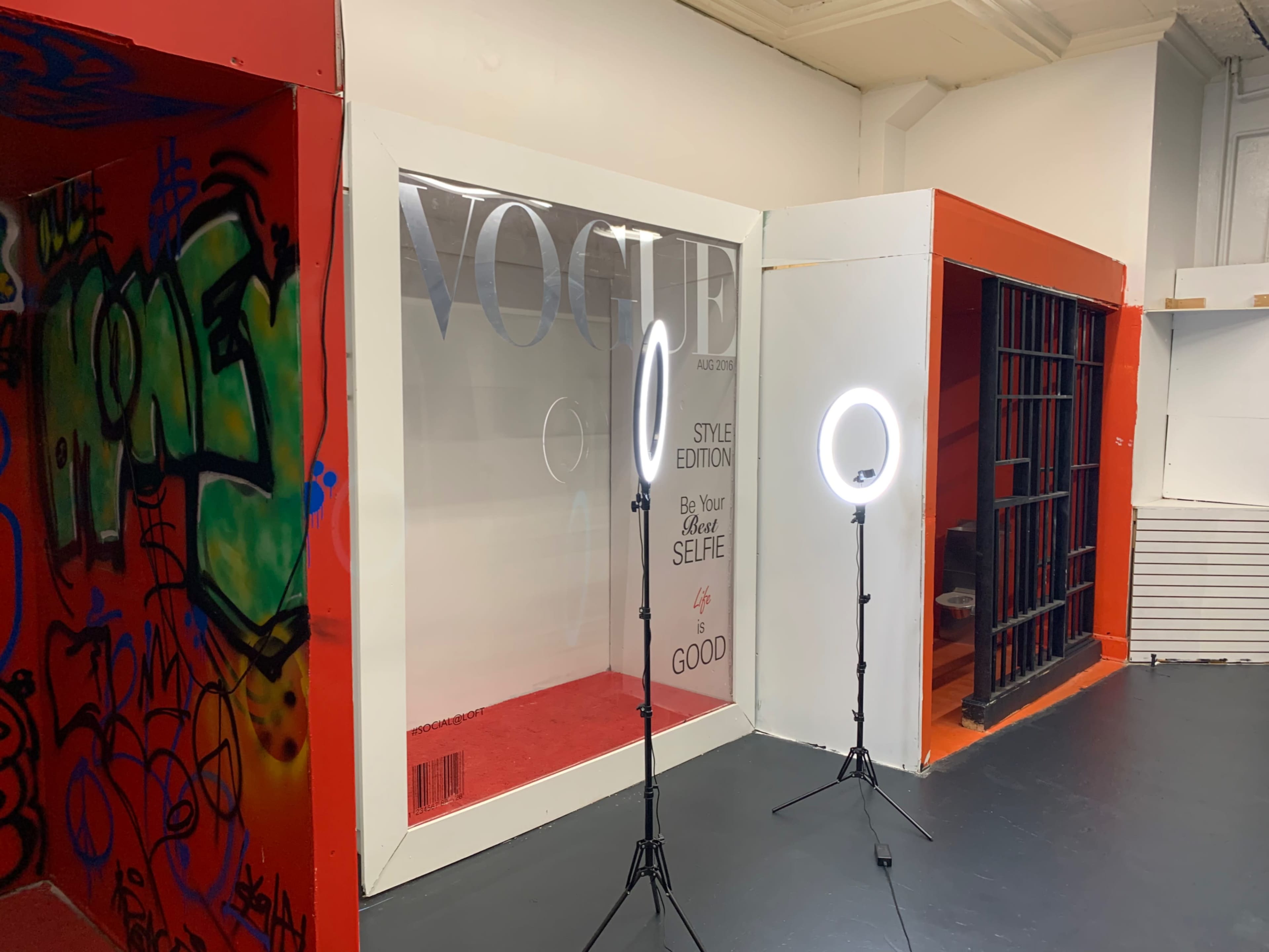 A stylized display area featuring a "VOGUE" backdrop, with two ring lights positioned in front on a black floor.