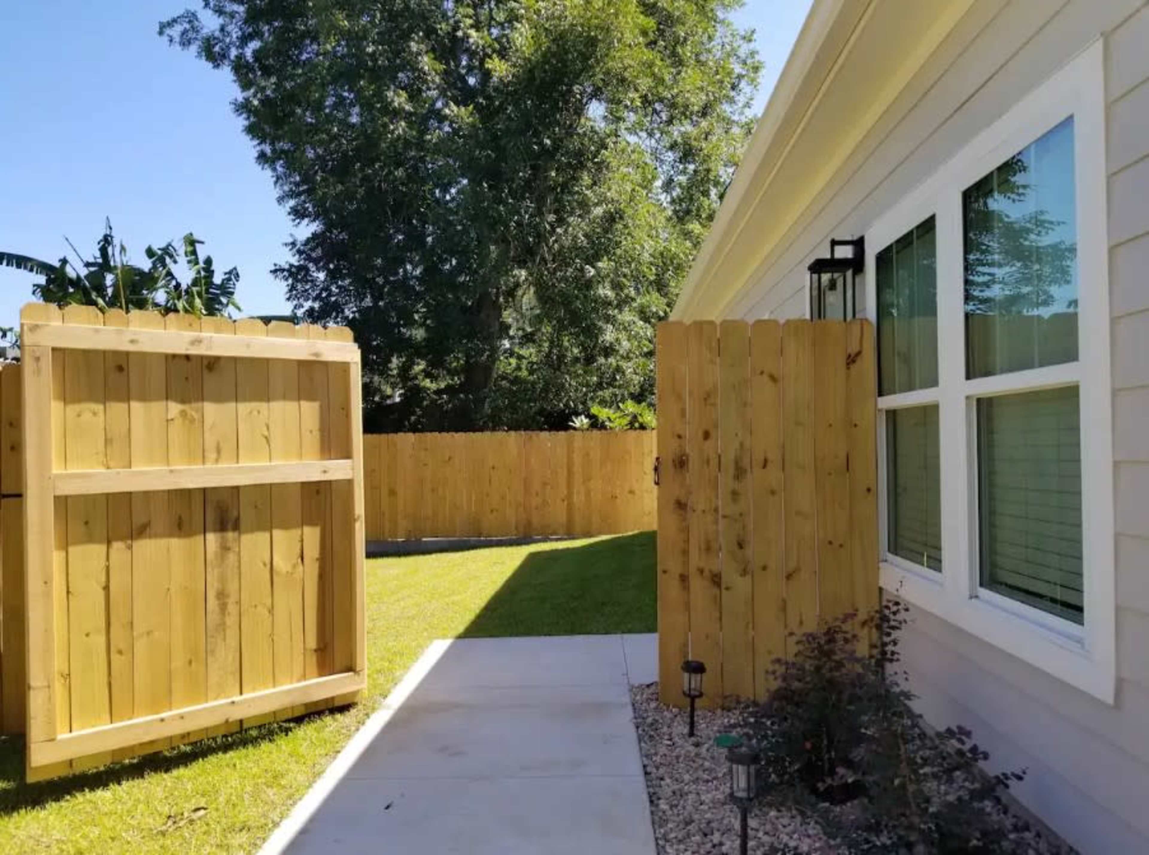 A wooden gate opens to a landscaped yard with grass and a fence made of wooden planks.