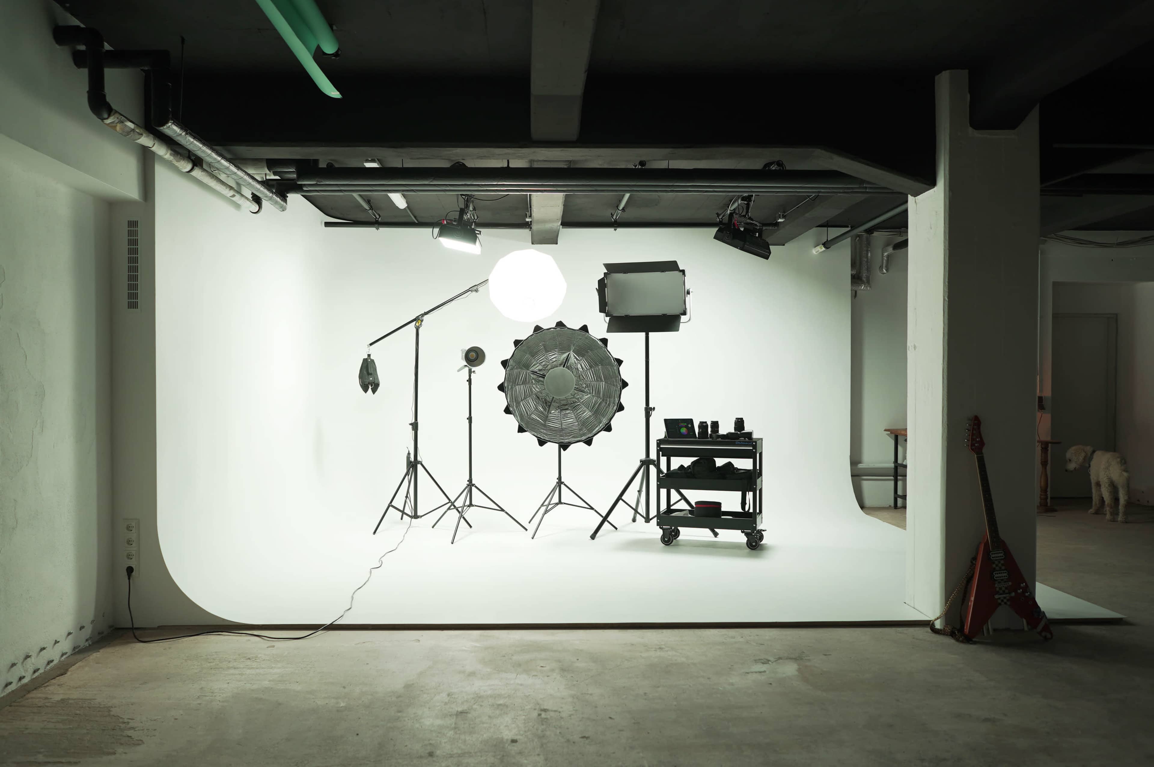 A photography studio setup featuring a backdrop, various lighting equipment, and a cart with photography accessories.