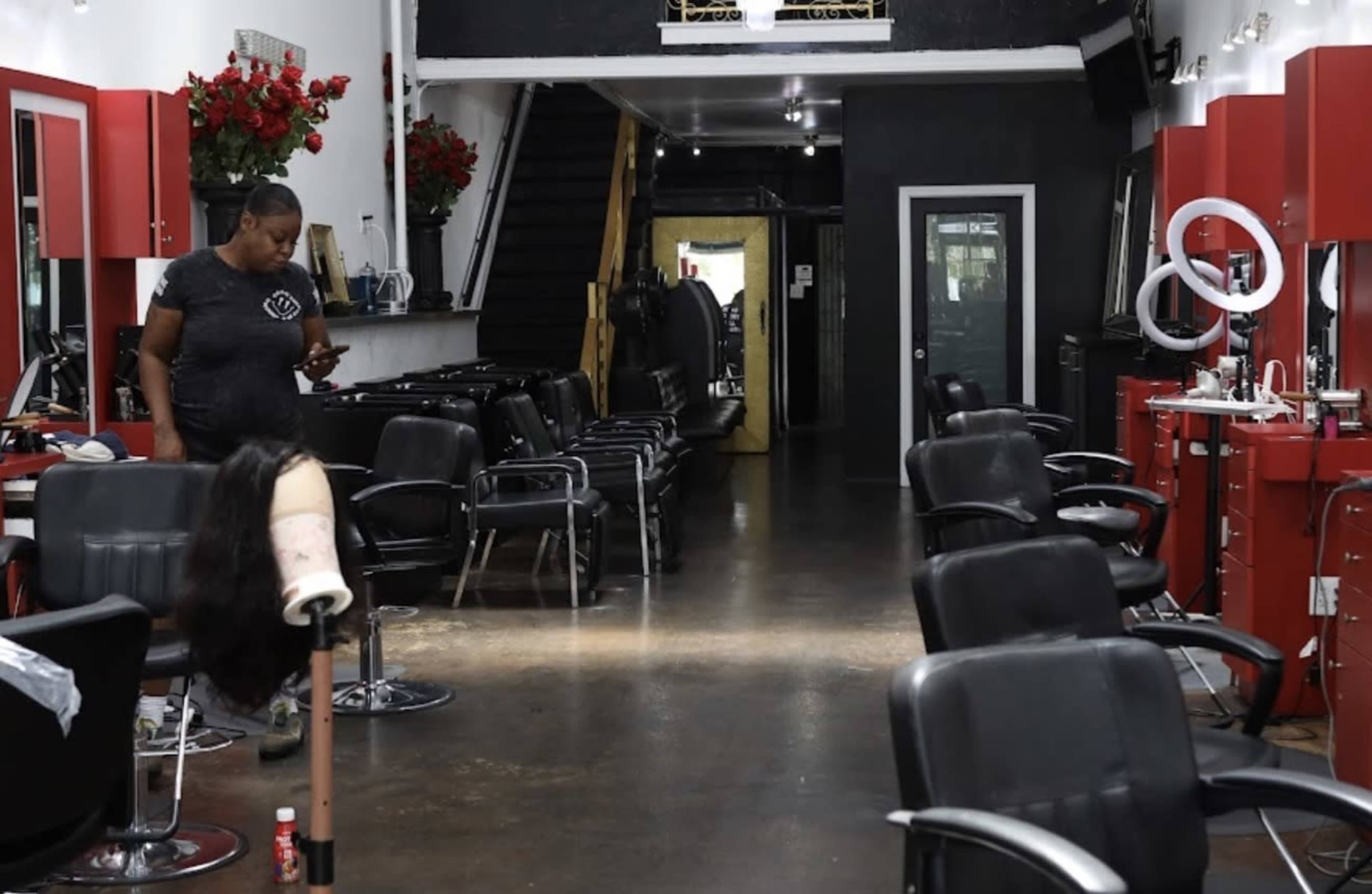 A hair salon features several styling stations, empty chairs, and a stylist checking her phone near the entrance.