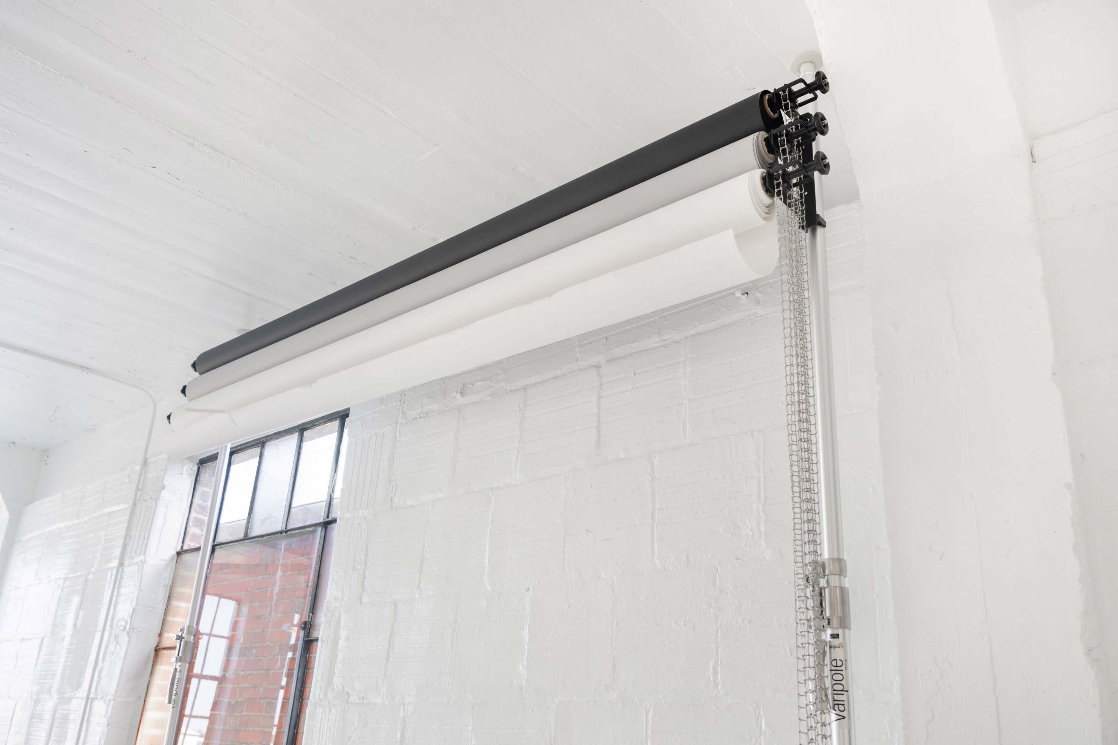 A wall-mounted roll of paper backdrop in a well-lit room with white walls and large windows.