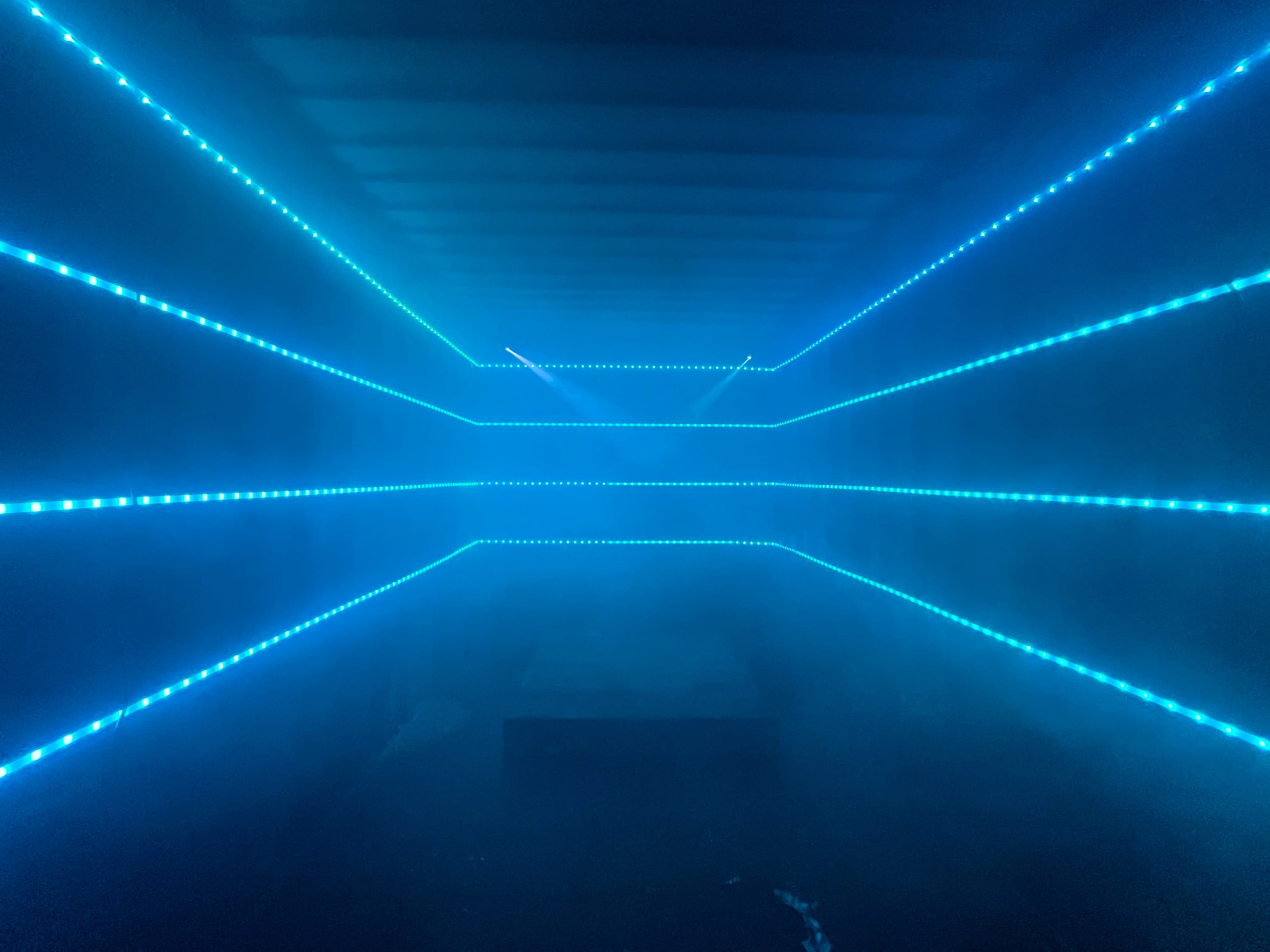 A dark corridor illuminated by horizontal blue LED lights and a haze of mist.