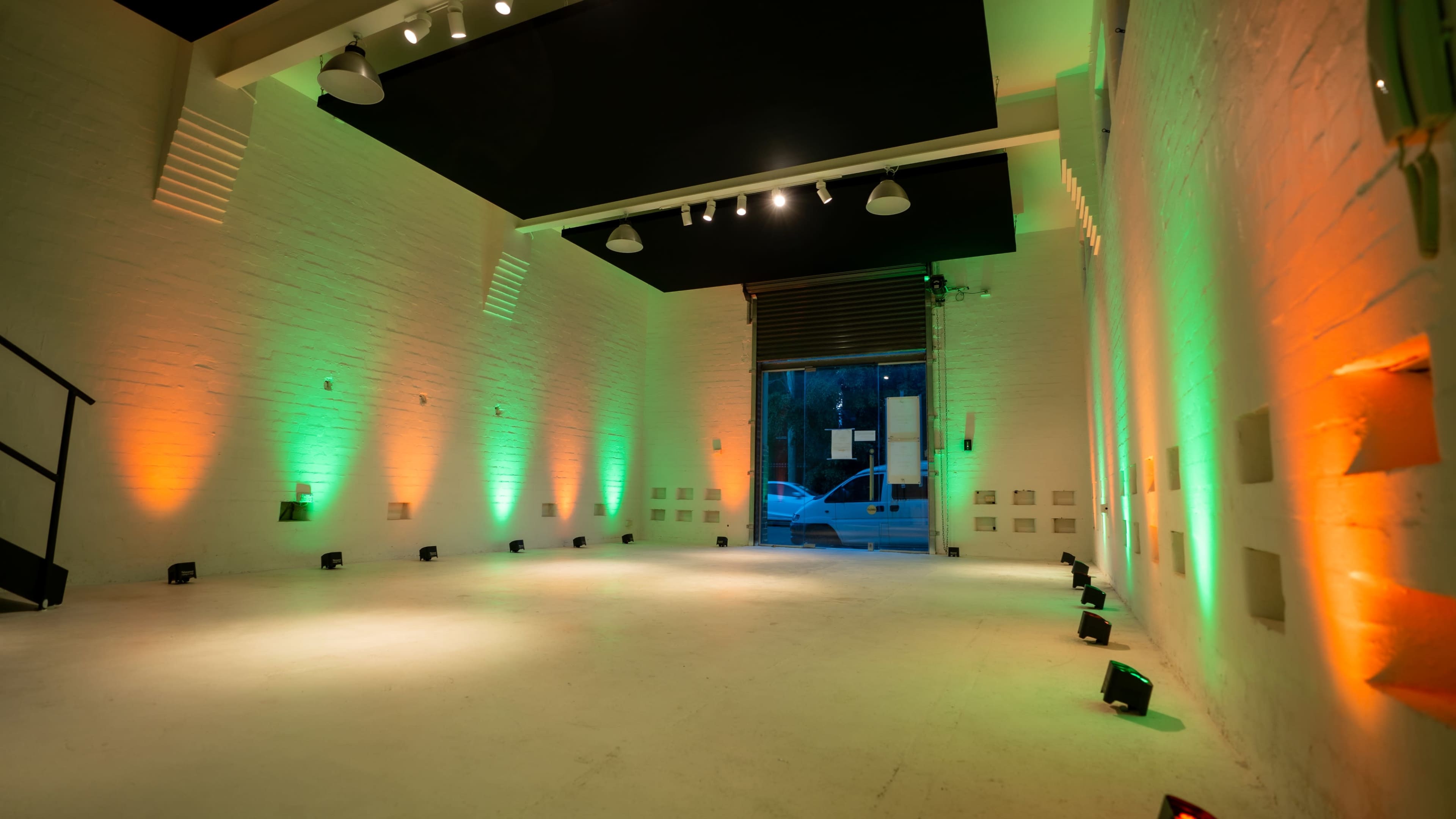 The interior of a spacious, well-lit room features green and orange lighting along the walls, with an open entrance visible at the far end.