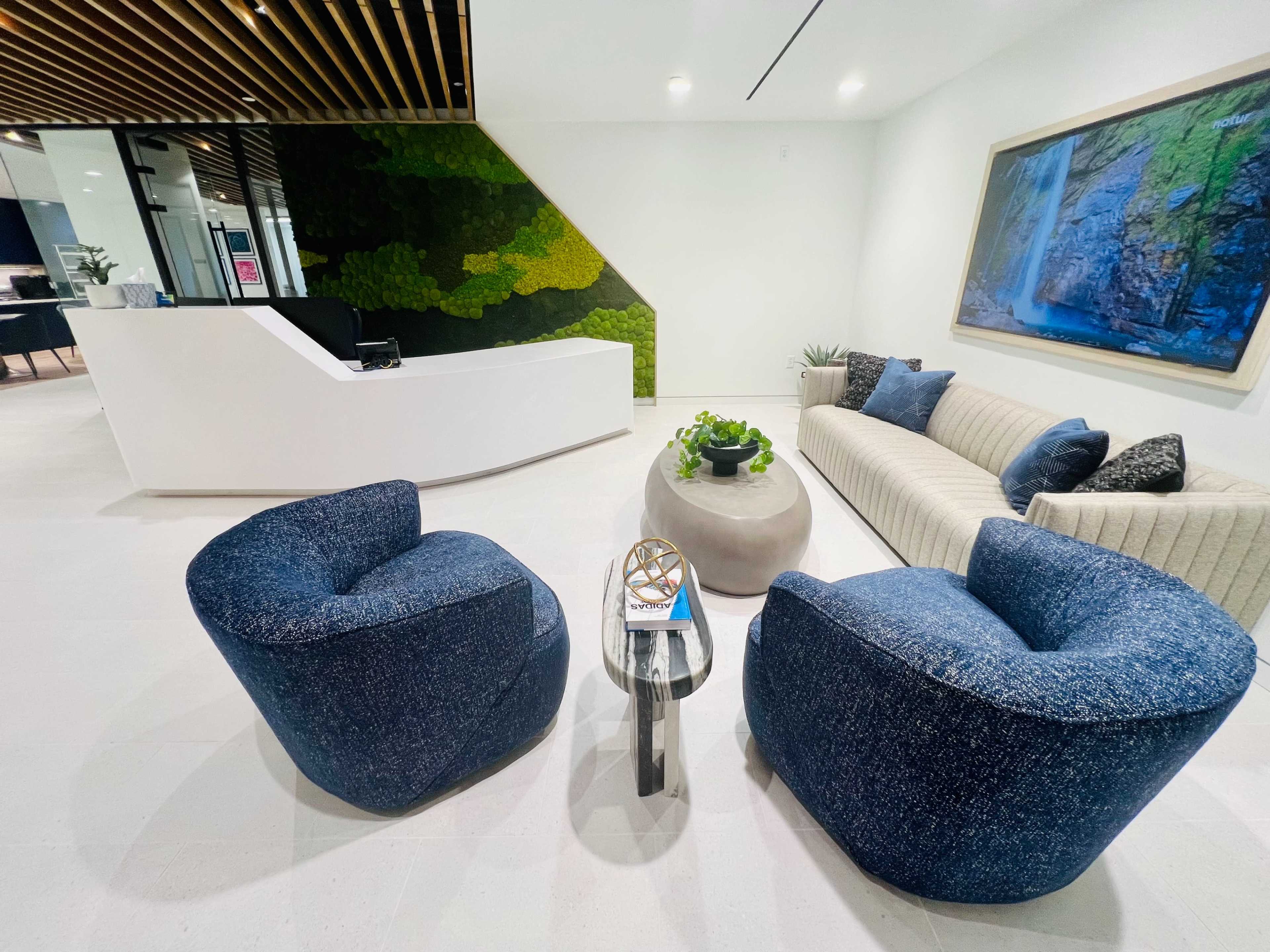 A modern reception area featuring a sleek front desk, a sofa, two rounded chairs, a coffee table, and a wall adorned with green decor.