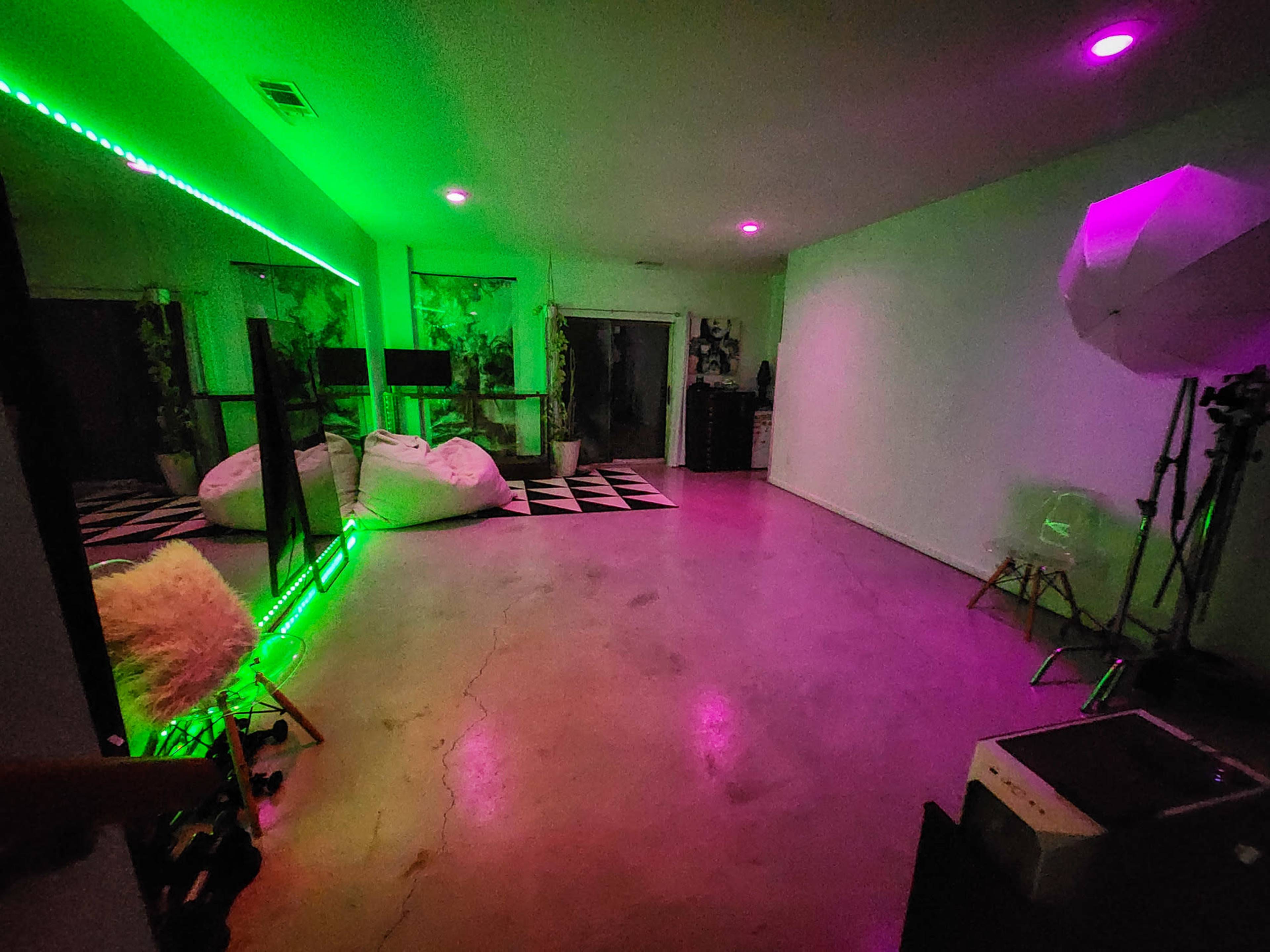 The image shows a modern room with a glossy concrete floor, colorful lighting, and a mix of furniture including bean bags and a photography backdrop setup.