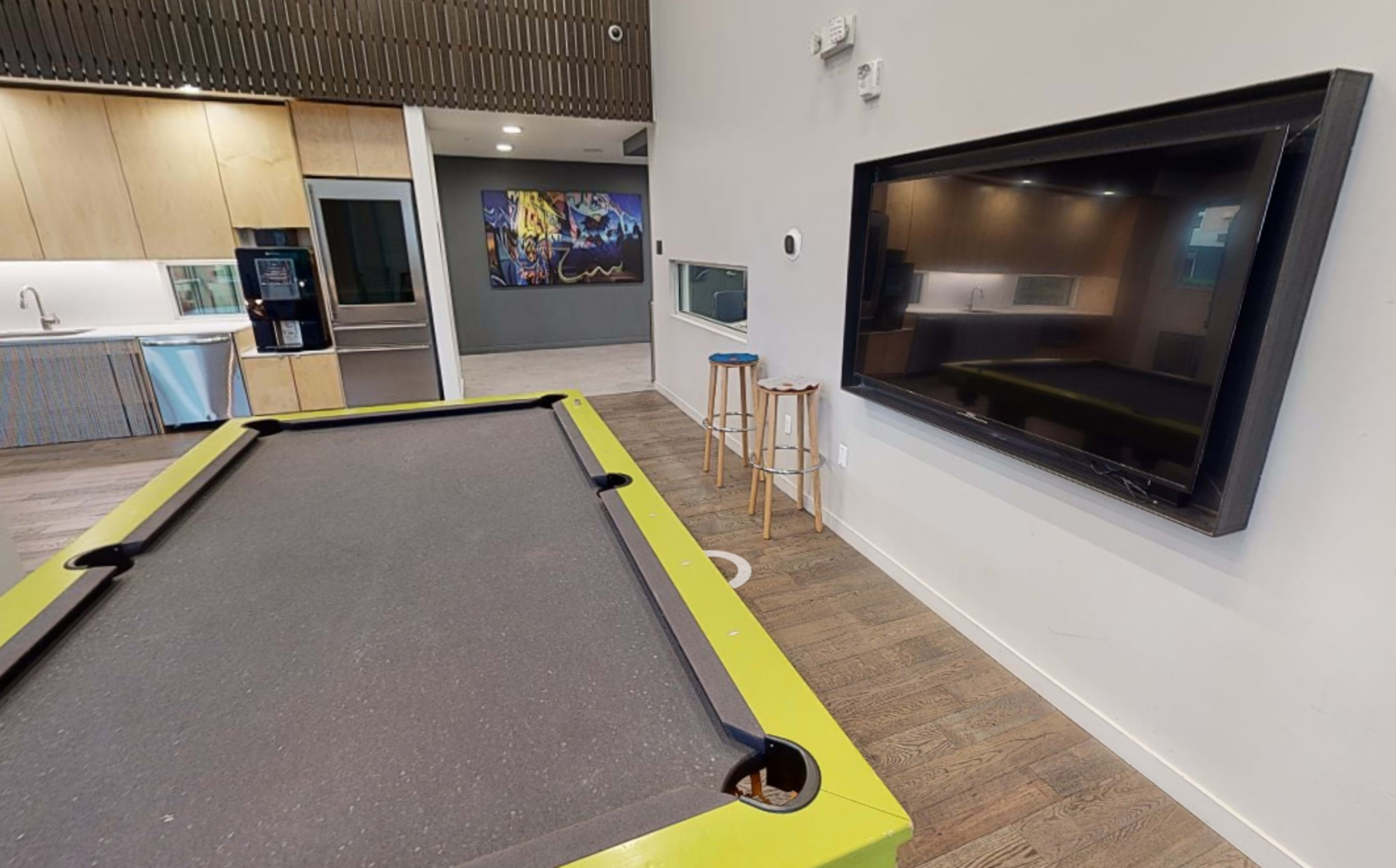 A game room features a green pool table next to a large wall-mounted television and modern cabinetry.