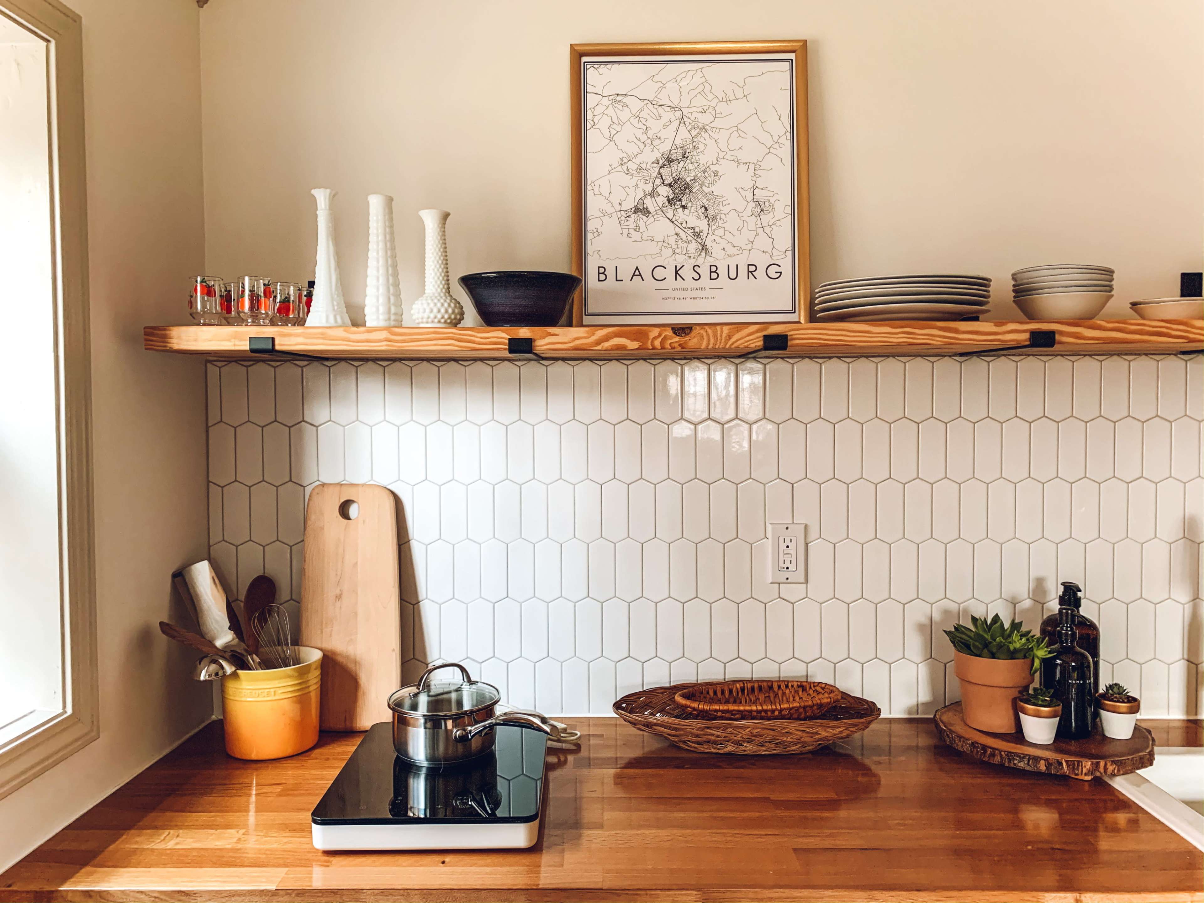 A kitchen countertop with a stove, cooking pot, wooden cutting board, decorative shelves, and potted plants.