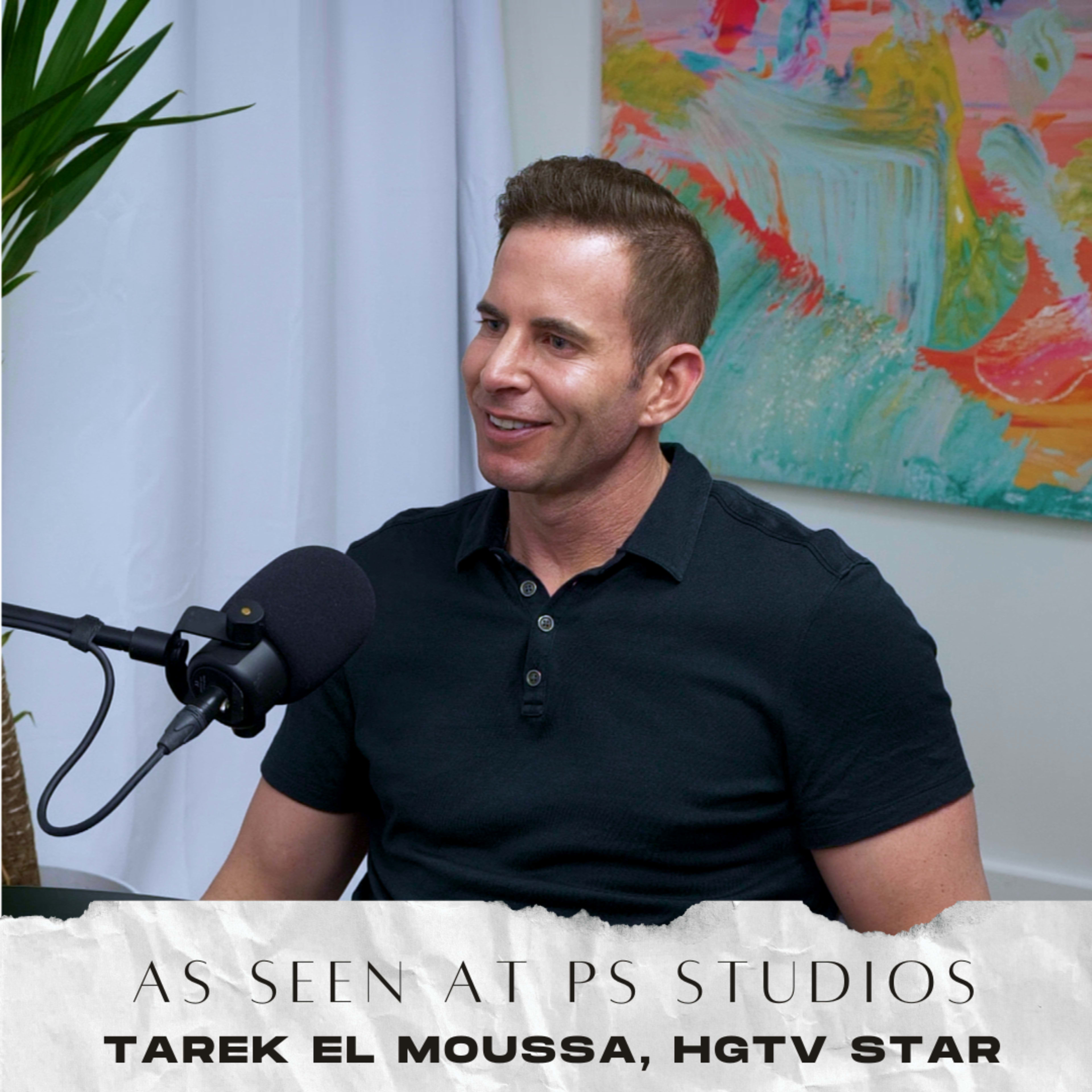 A man is sitting in a studio setting, speaking into a microphone with a colorful painting in the background.