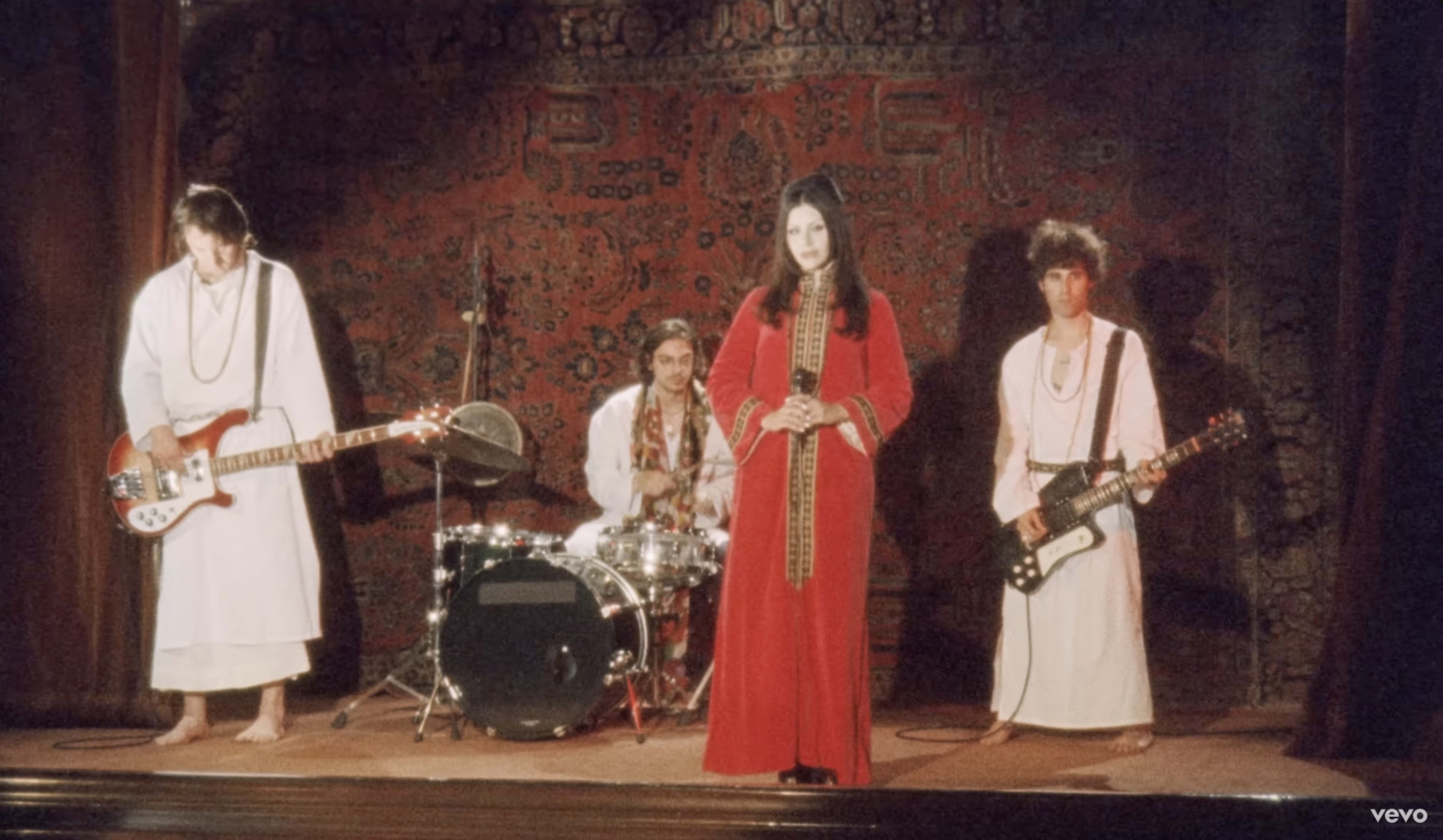 A band dressed in traditional clothing performs on stage in front of a decorative backdrop.