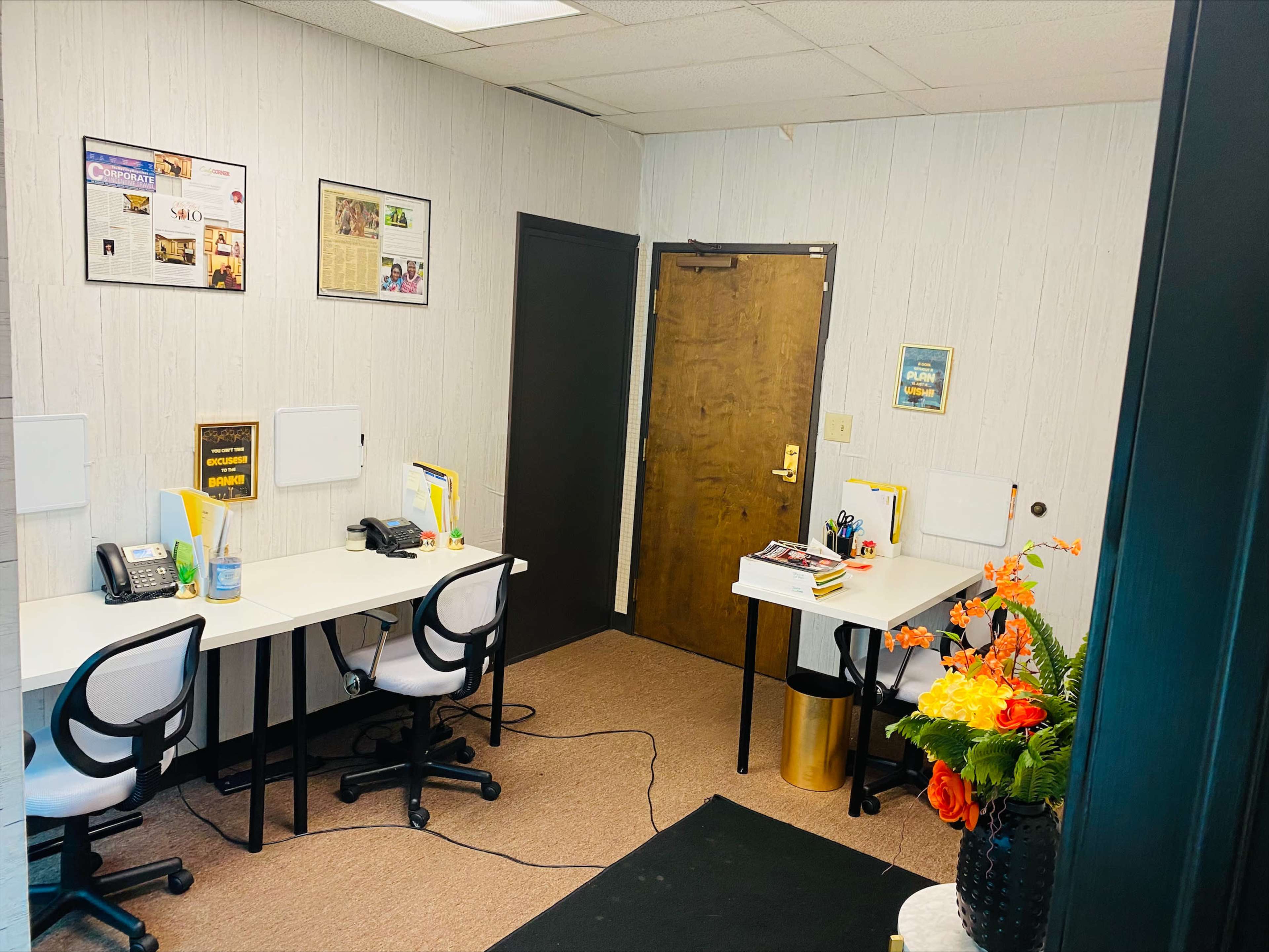 A small office space with two desks, each equipped with a phone and office supplies, and a doorway leading to another room.