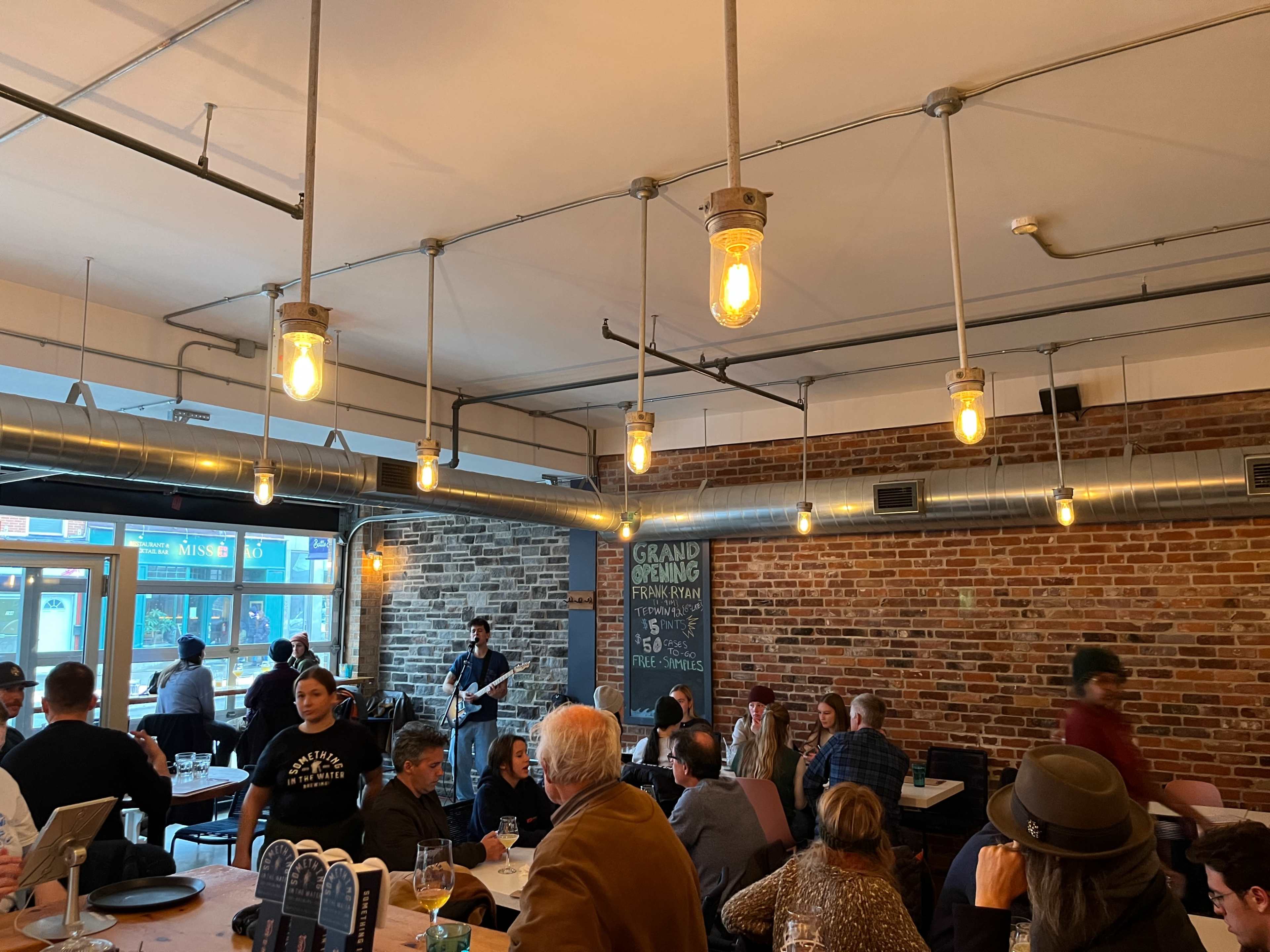 A bustling restaurant interior with exposed brick walls, warm lighting, and patrons enjoying food and a live band performance.