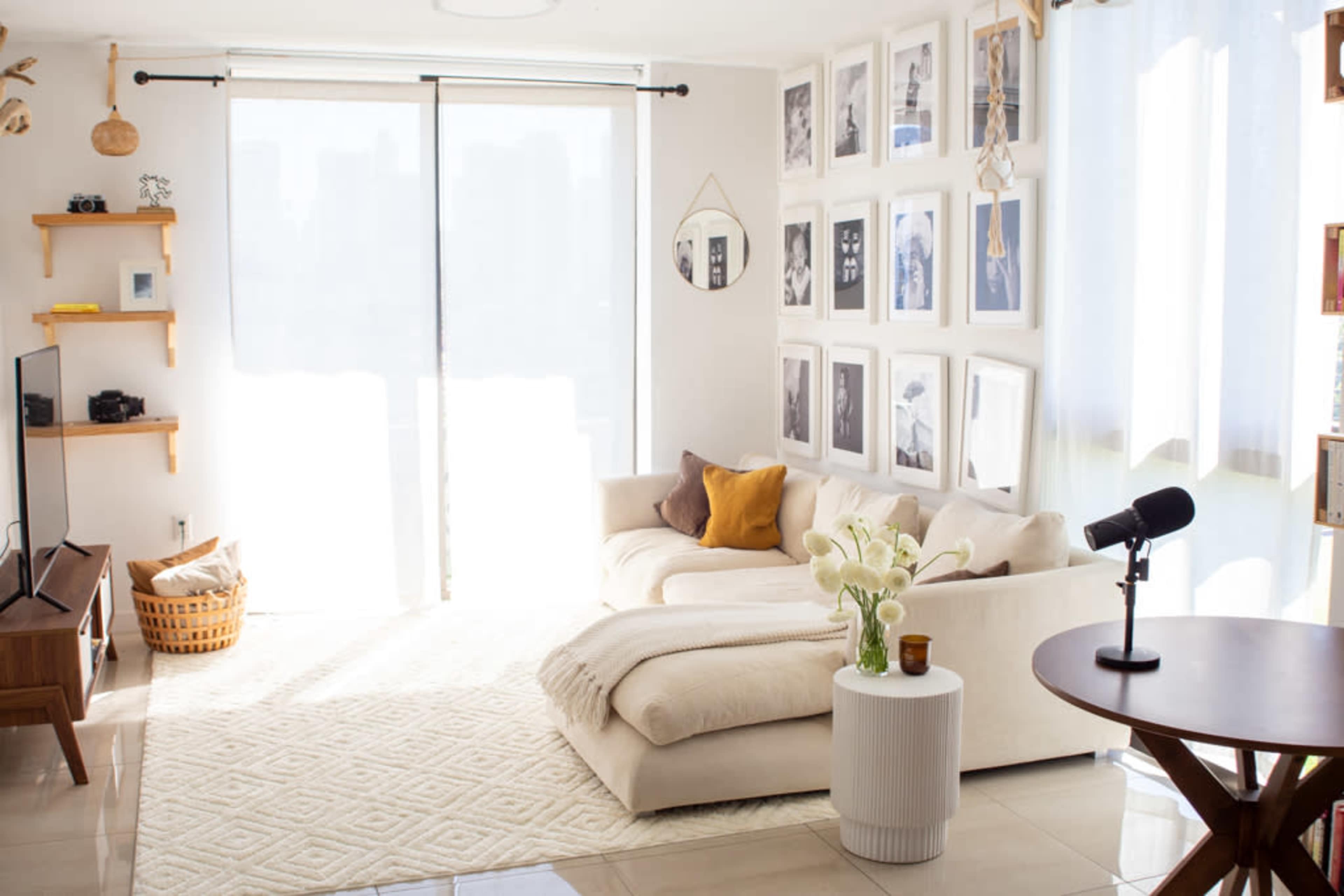 A bright living room features a large white sectional sofa, a round side table with a vase of flowers, and a wall adorned with framed black and white photographs.