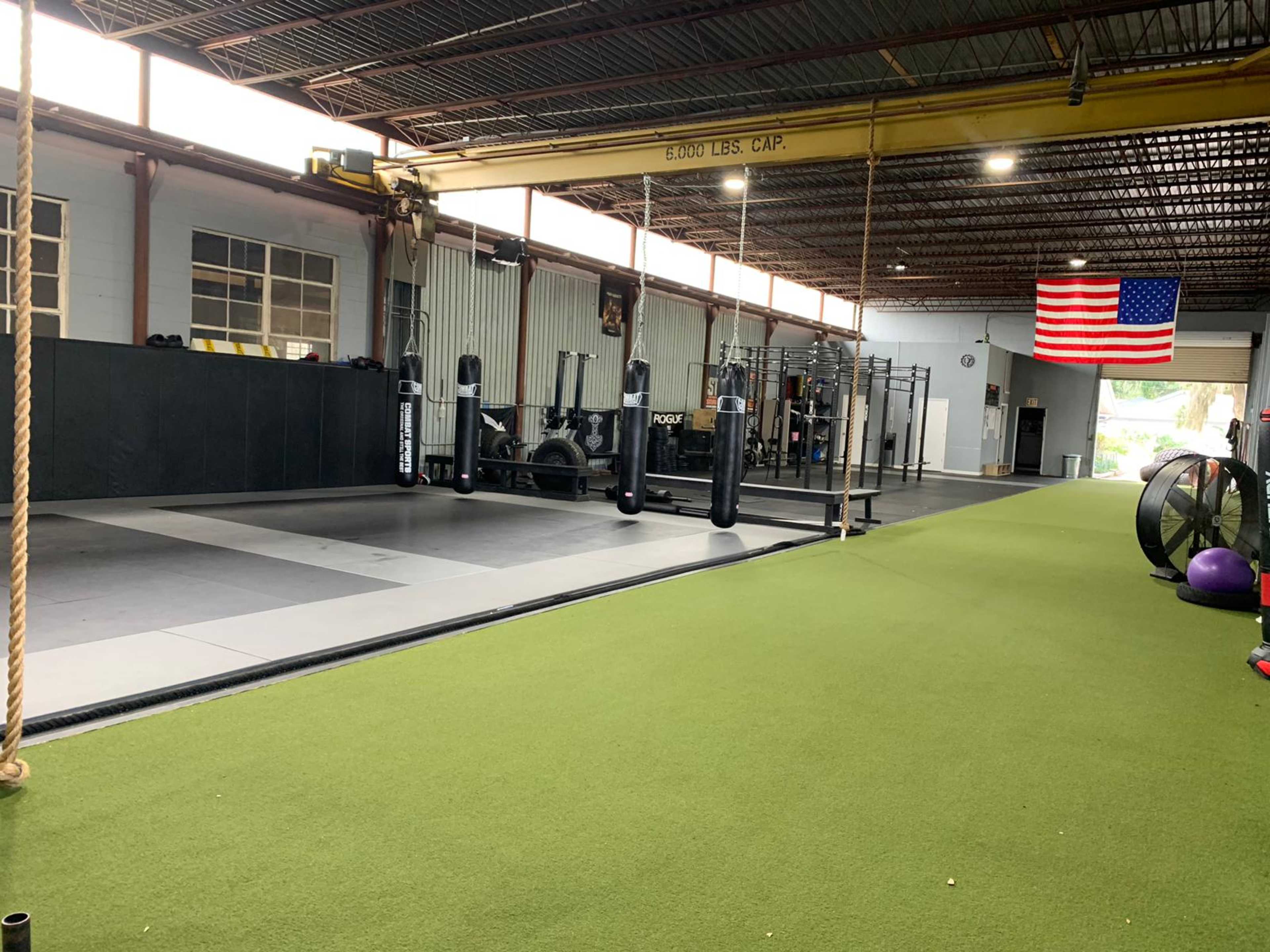 A spacious gym with turf flooring, weightlifting equipment, and an American flag hanging on the wall.