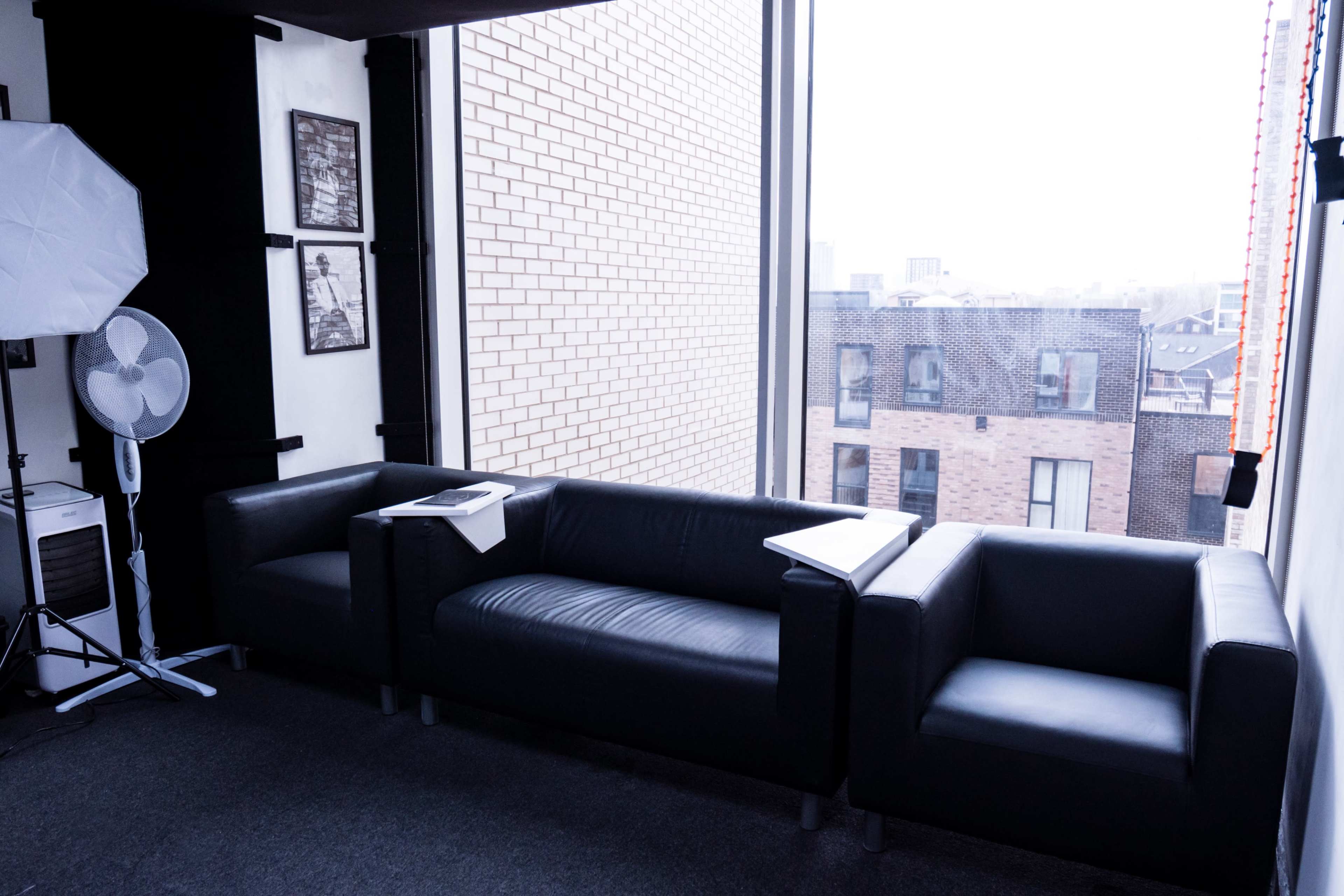 A modern, minimalist lounge area features two black leather sofas and a small side table beside a large window overlooking city buildings.