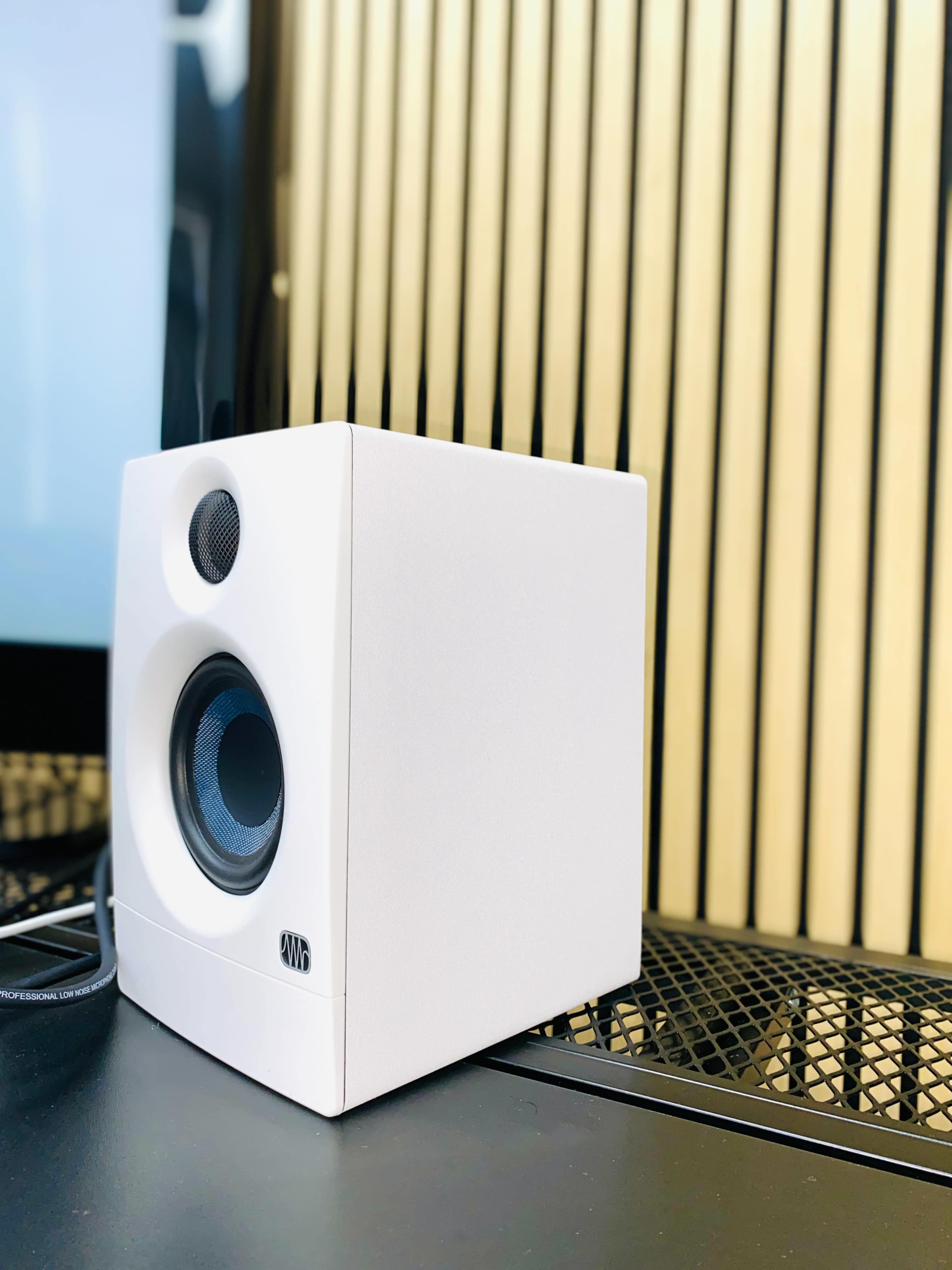 A white speaker is positioned on a black surface with a striped background.