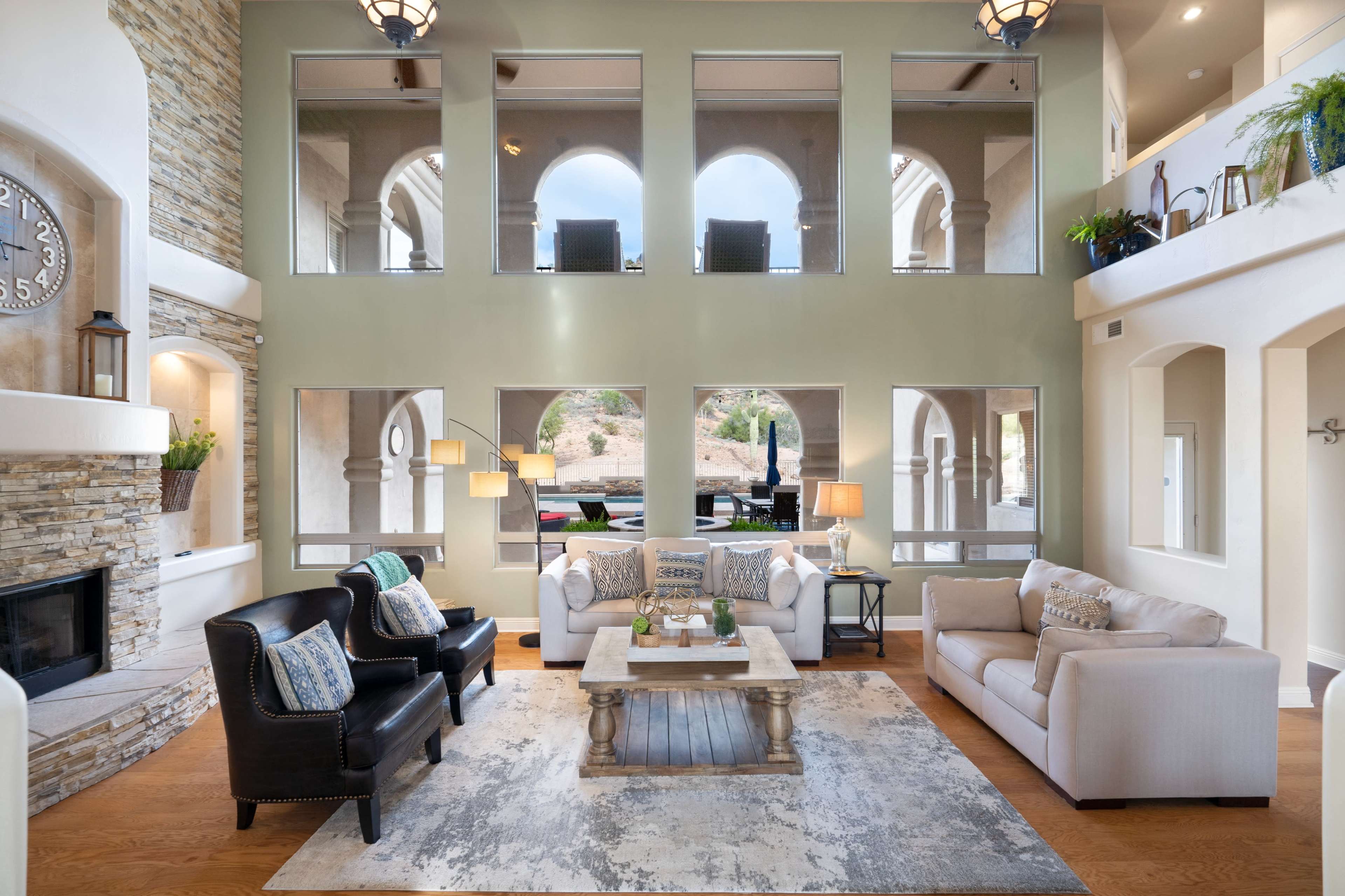 A spacious living room with high ceilings, large arched windows, two sofas, and a wooden coffee table.