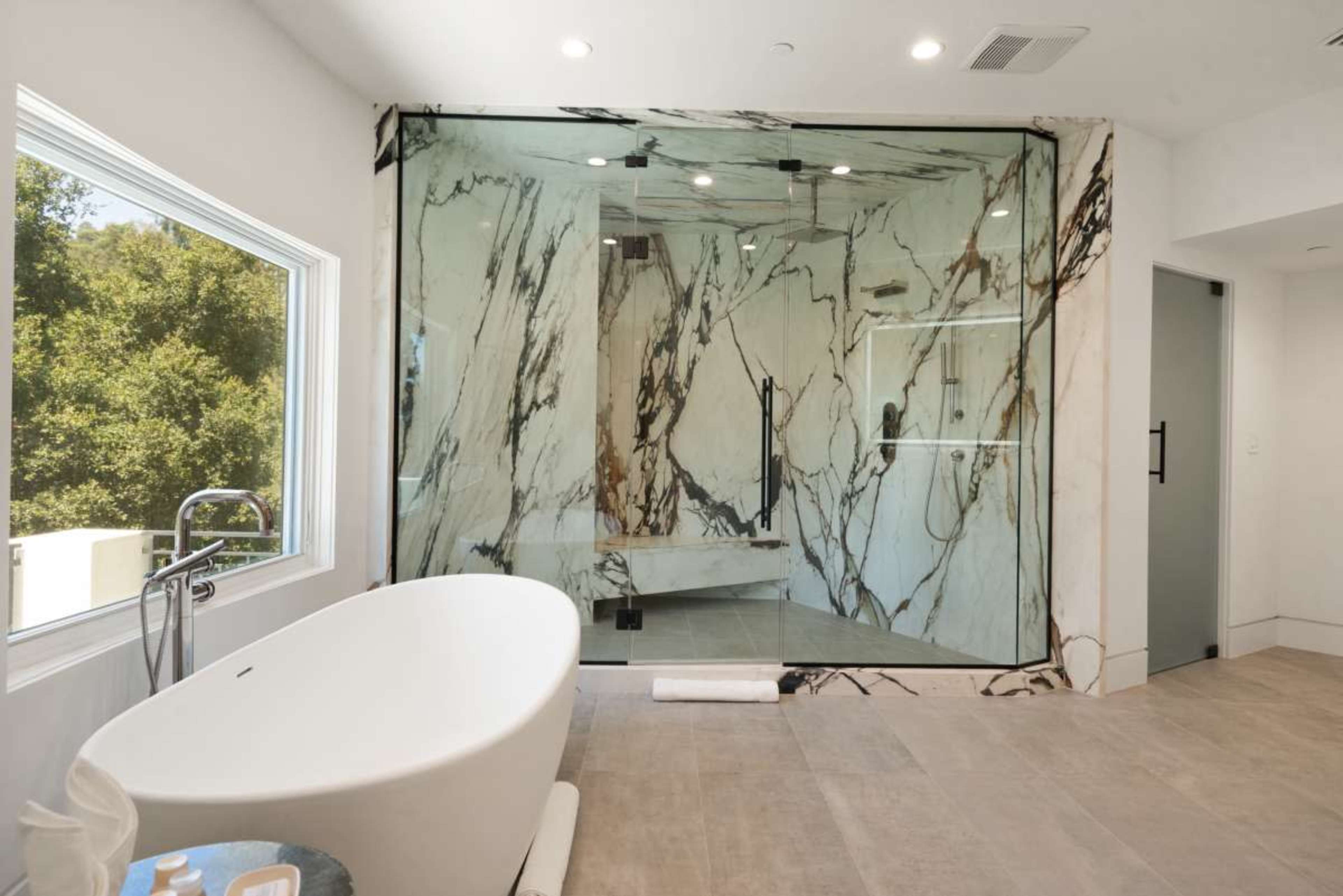 A modern bathroom features a large freestanding bathtub and a glass-enclosed shower with marble walls.