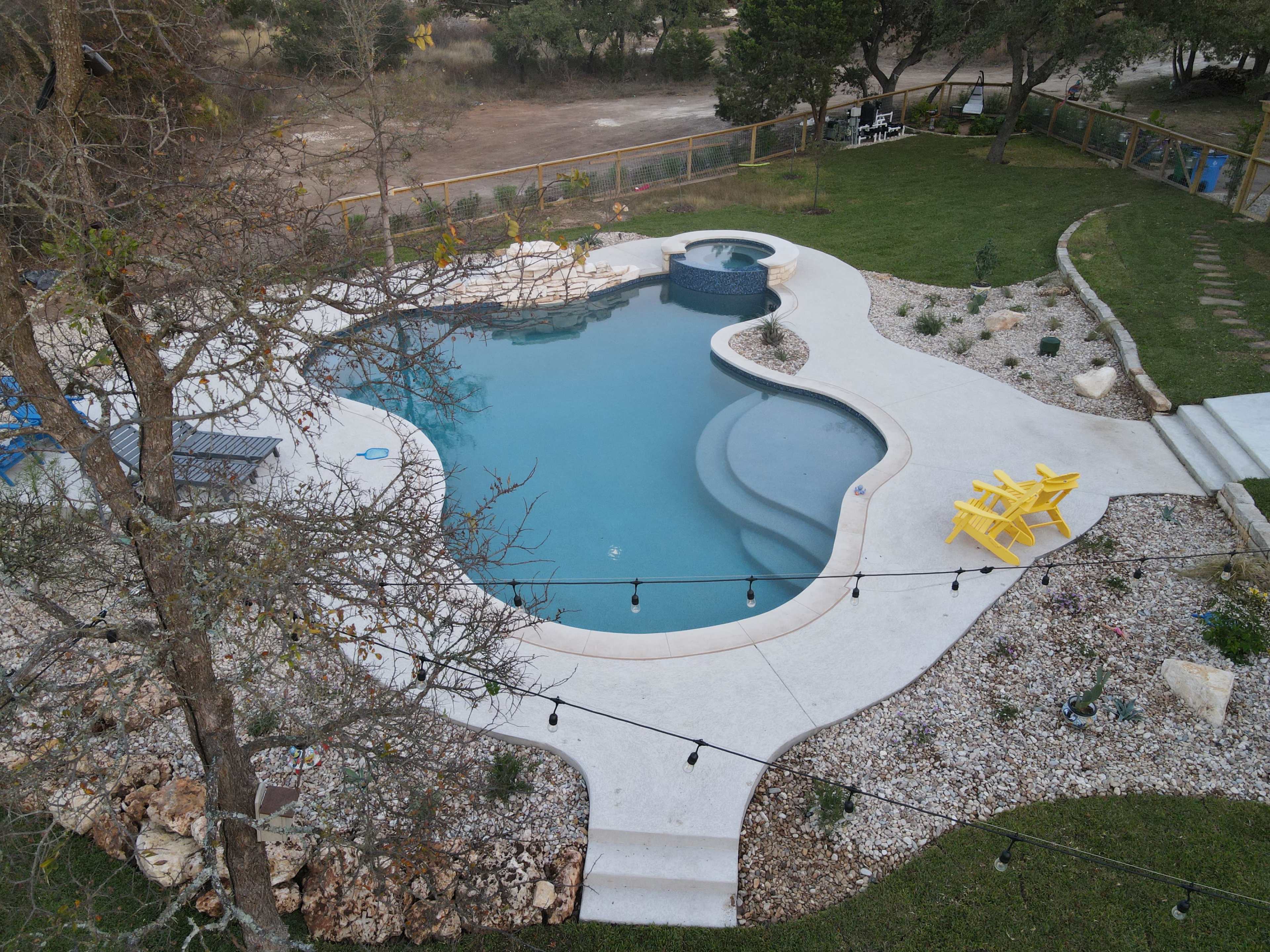 A rectangular swimming pool with a spa and surrounded by a landscaped area featuring rocks, plants, and two yellow chairs.