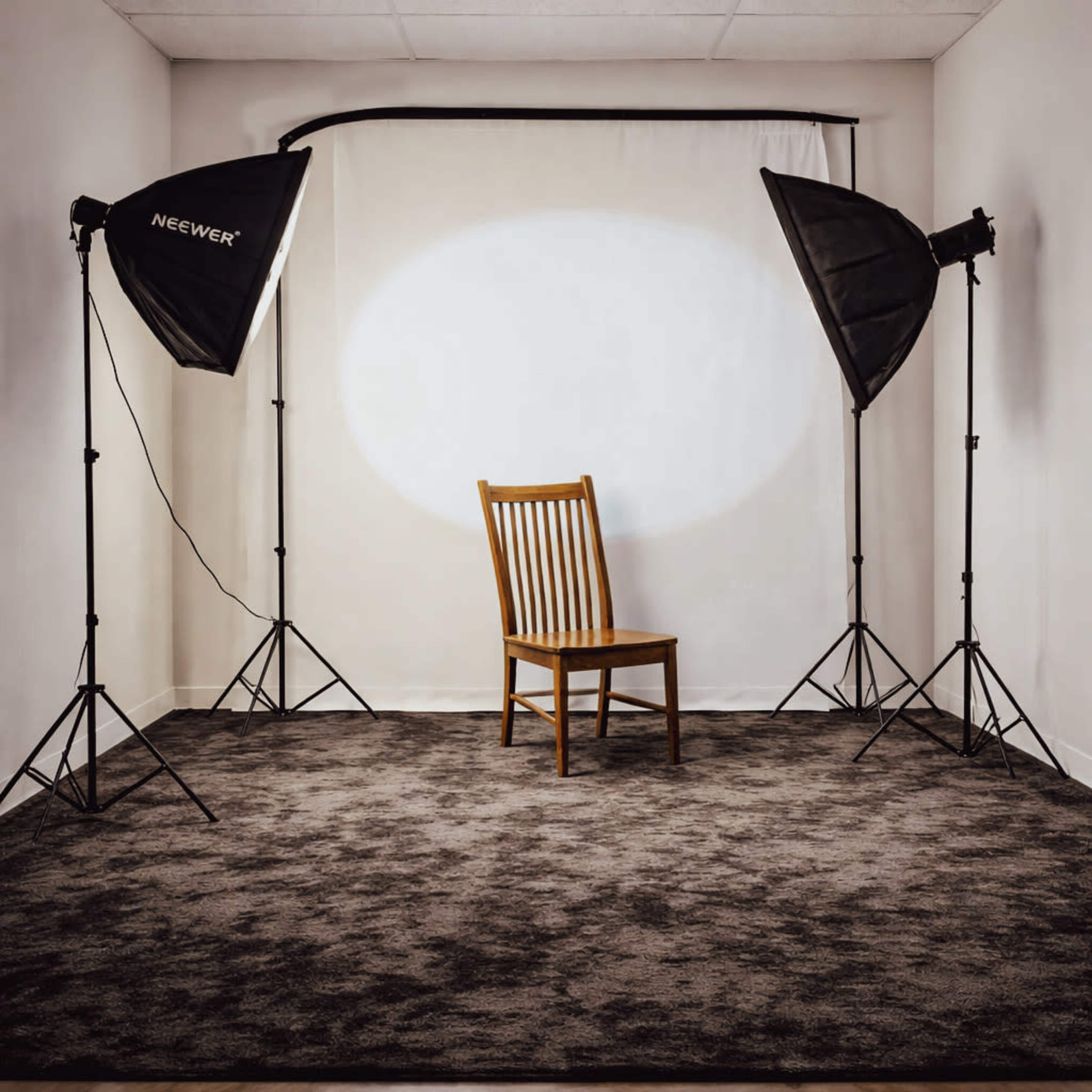 The image shows a wooden chair positioned in the center of a studio space, illuminated by two softbox lights on either side, with a neutral backdrop.