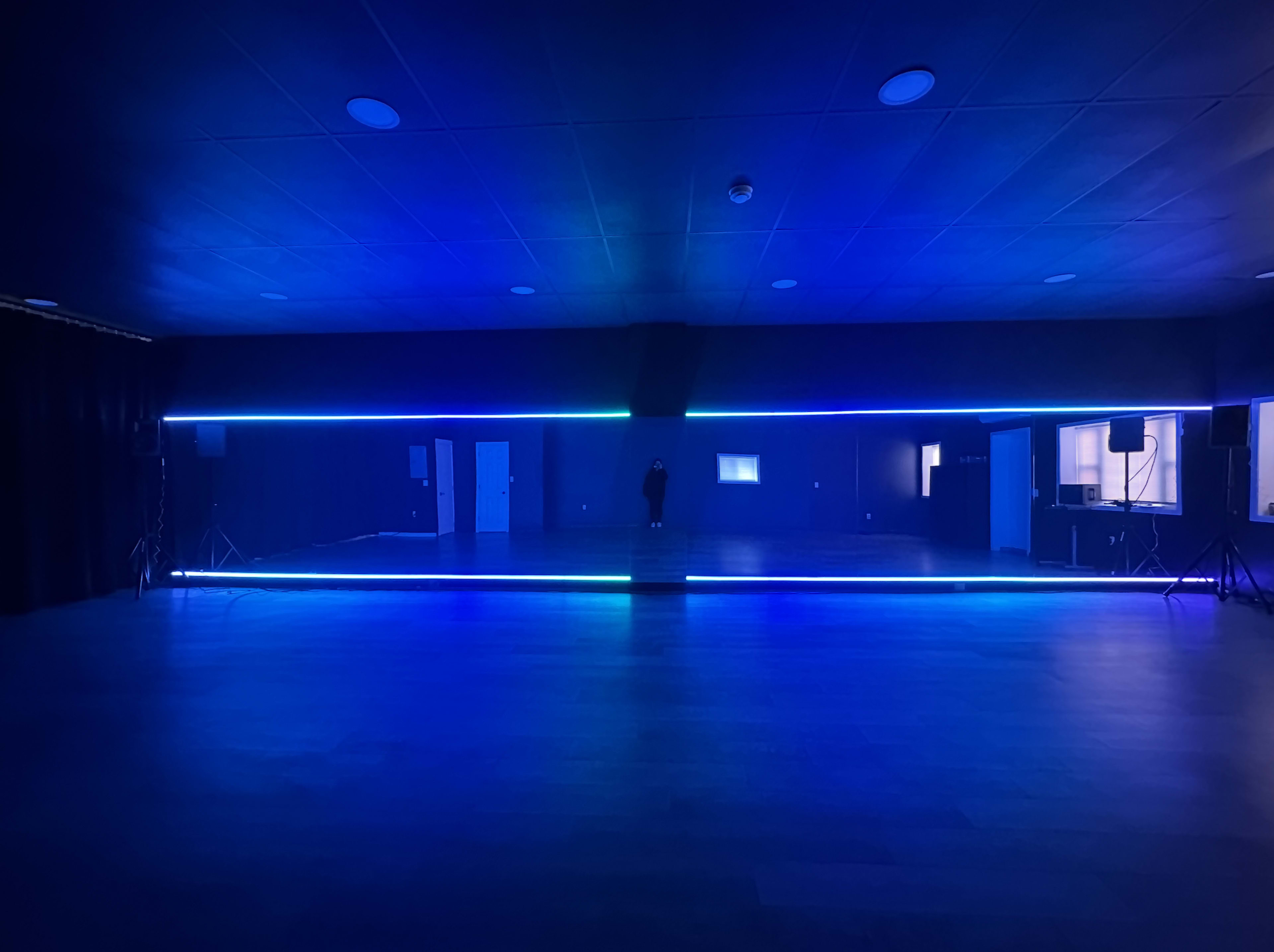 The image shows a dimly lit room with blue LED lights illuminating the edges of the walls and floor, creating a modern and stark atmosphere.