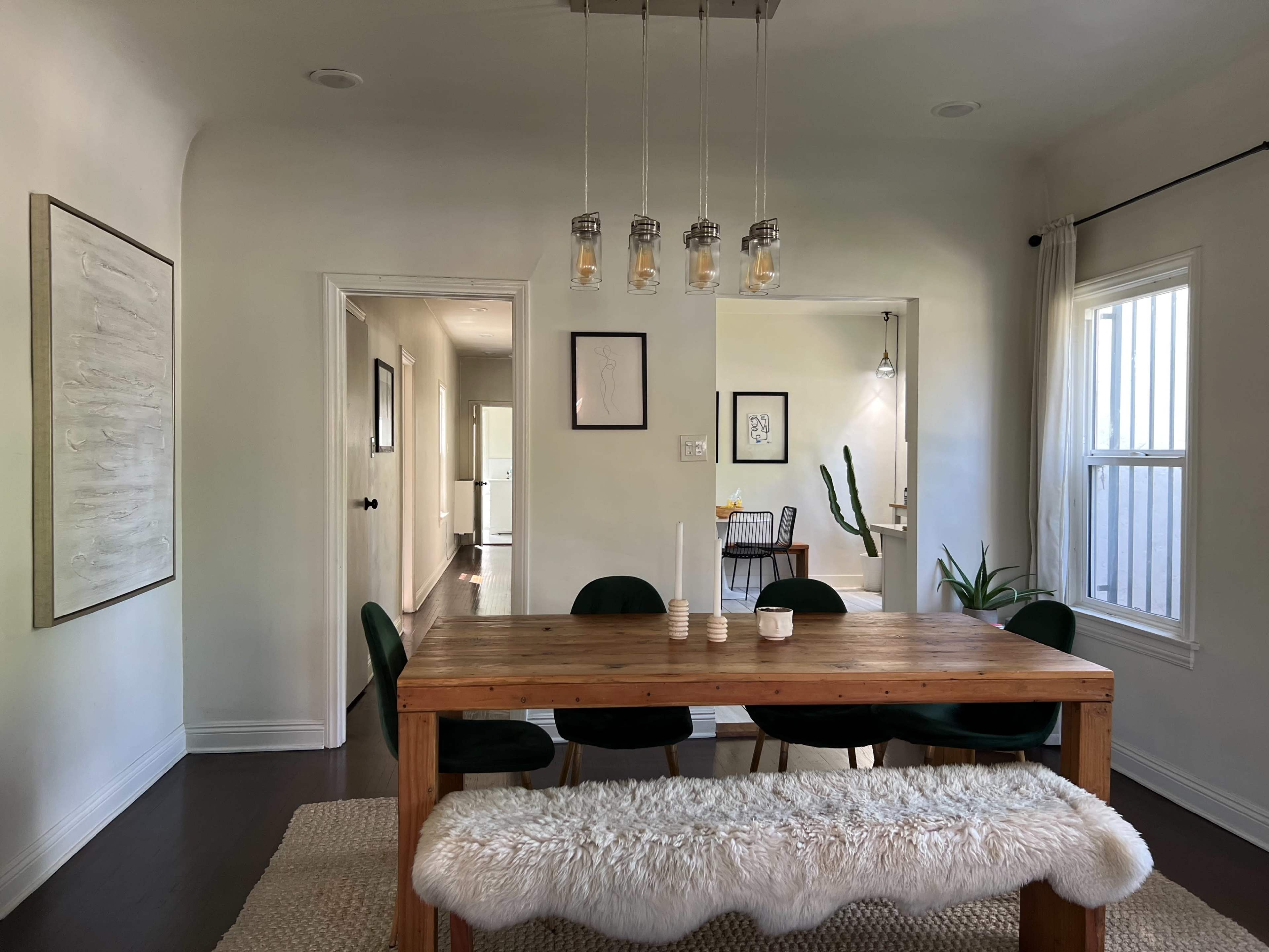 A wooden dining table surrounded by green chairs is set against a bright, minimalist interior with white walls and a rug.