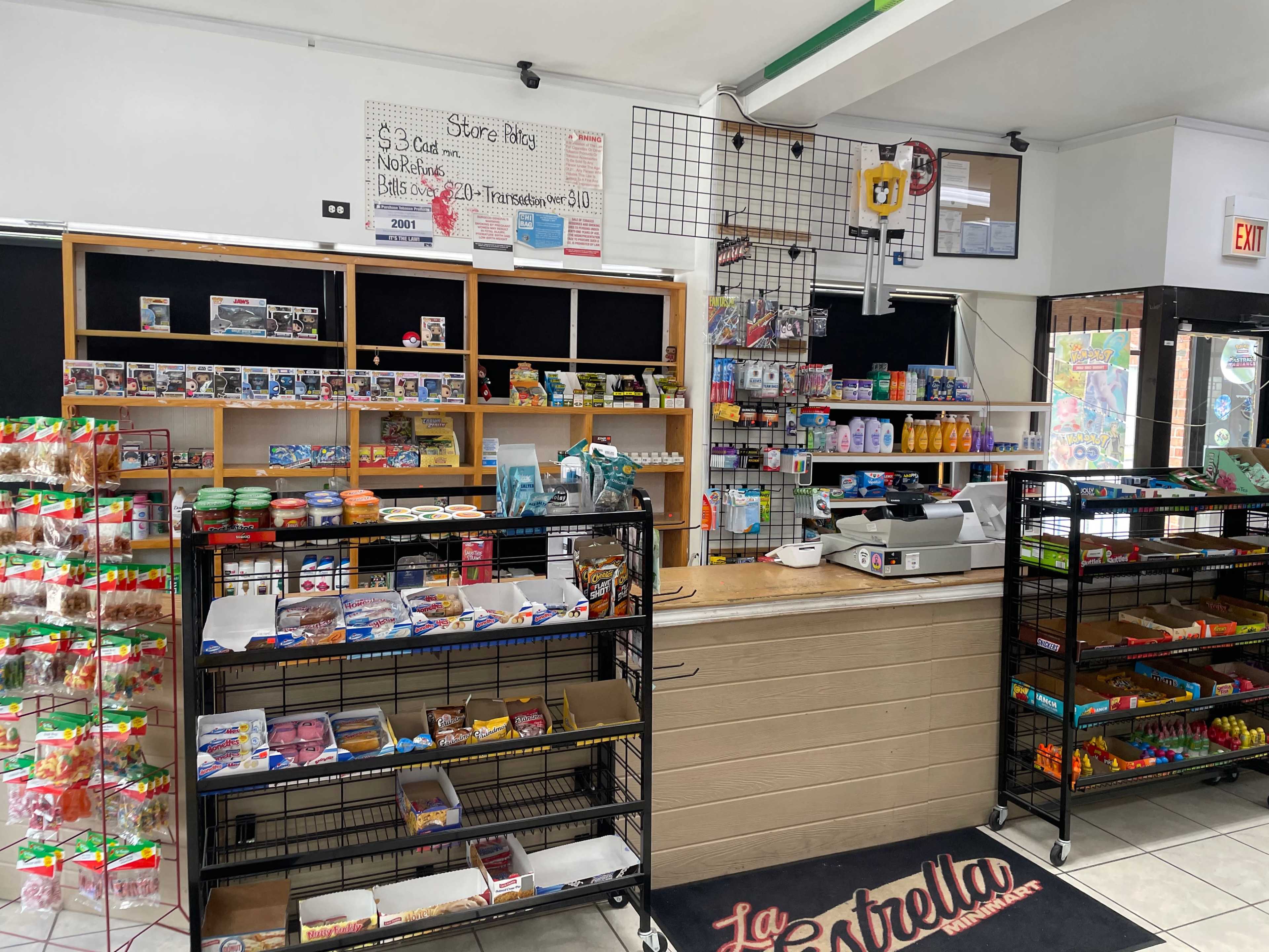 The interior of a small convenience store with shelves filled with snacks, beverages, and various products, alongside a checkout counter.