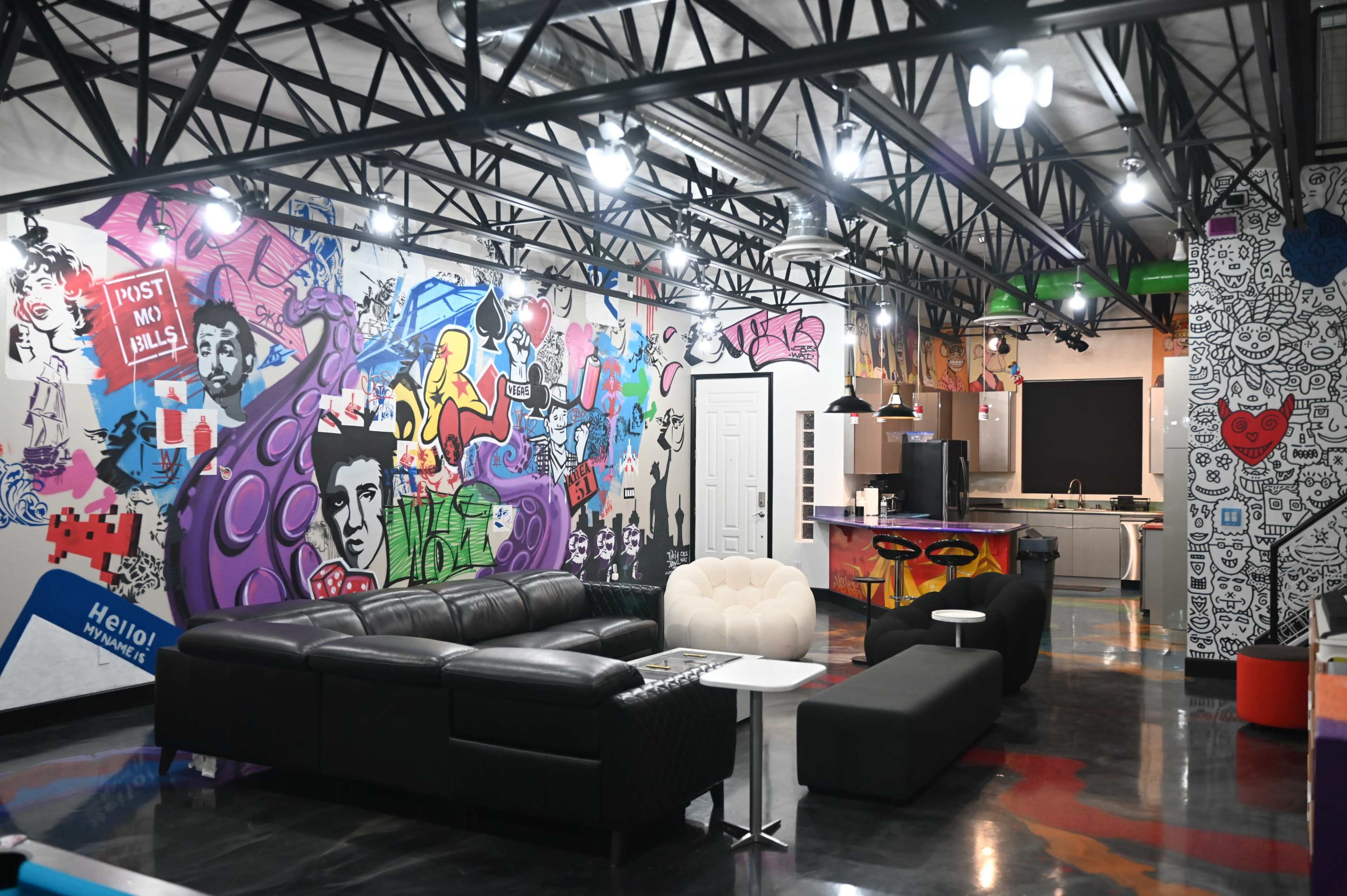 The image shows a modern lounge area featuring black and white furniture and colorful graffiti murals on the walls.