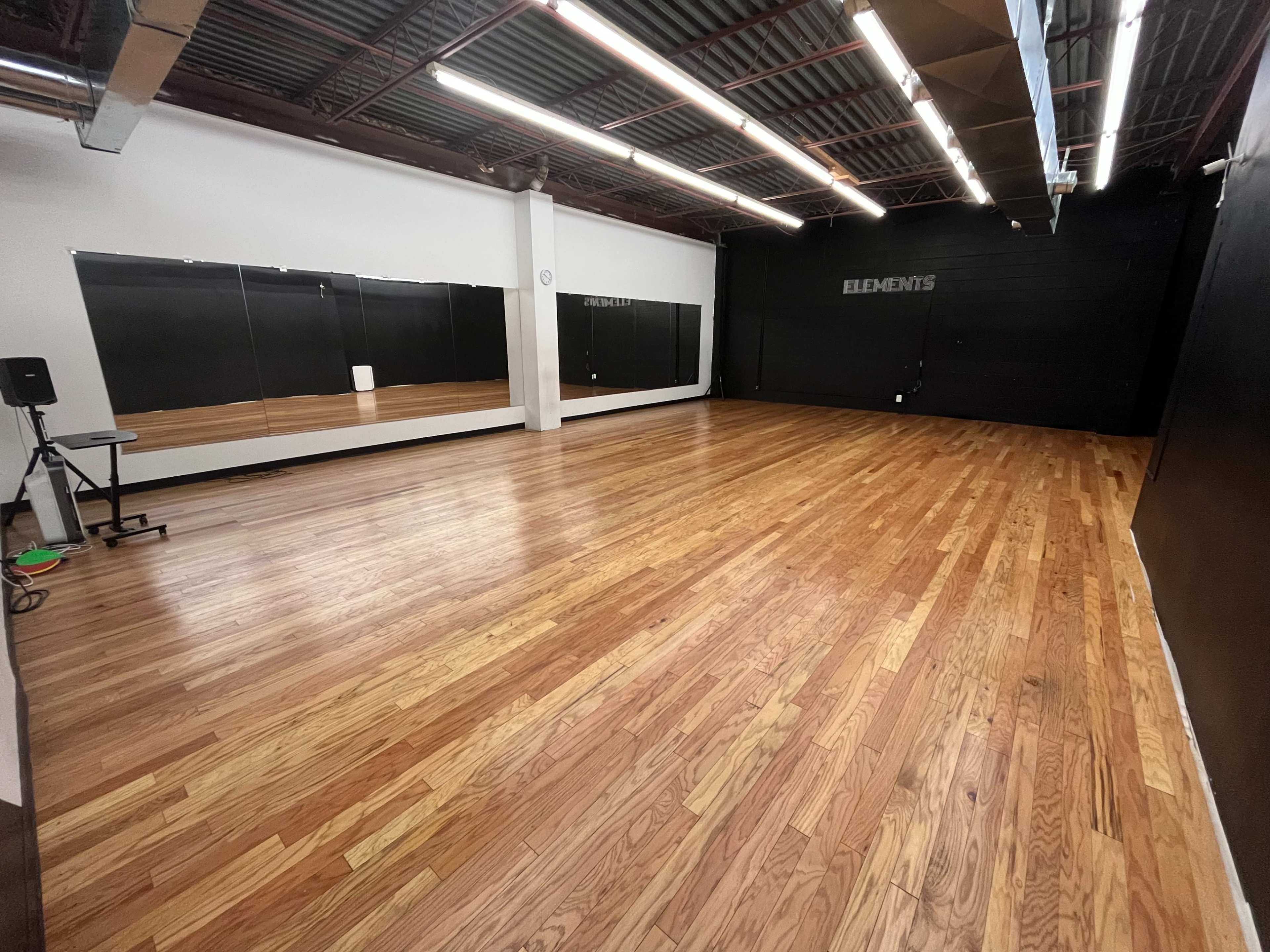An empty dance studio with wooden flooring and mirrors on one wall.