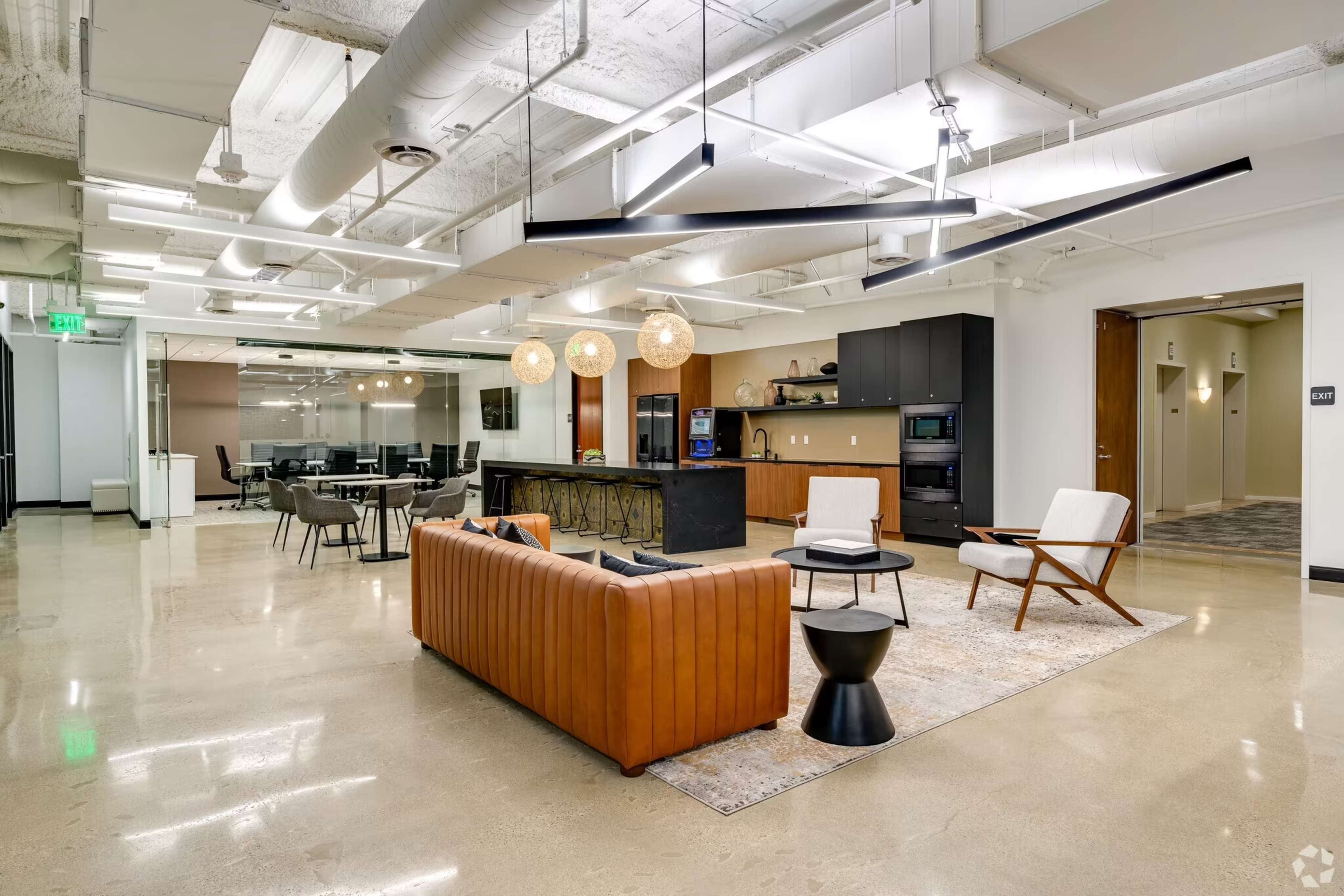 A modern office space featuring a lounge area with a leather sofa, two chairs, and a bar counter, along with a dining area equipped with tables and chairs.